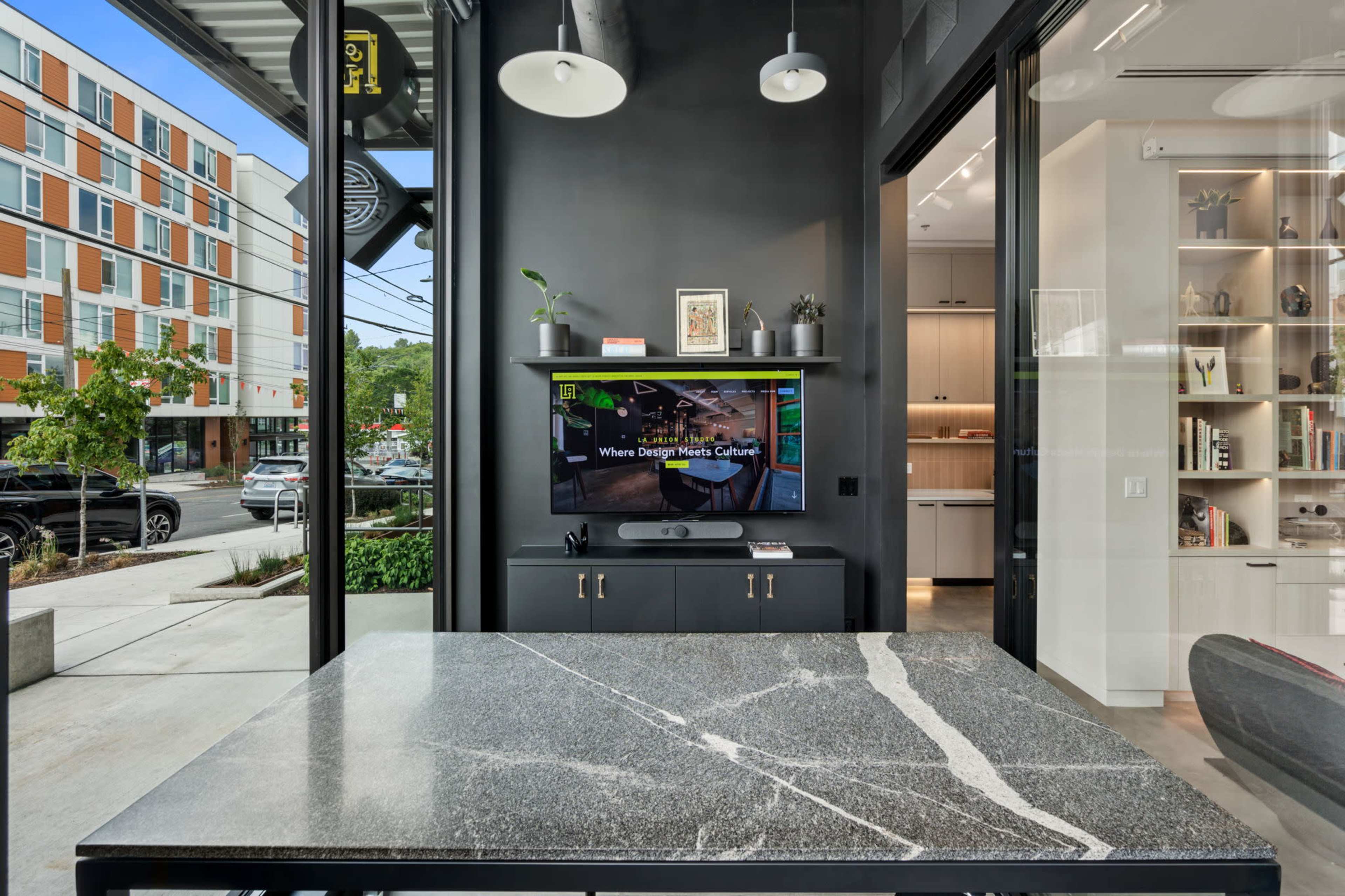 A modern interior features a large stone table in the foreground with a wall-mounted TV displaying a design-related message behind it.