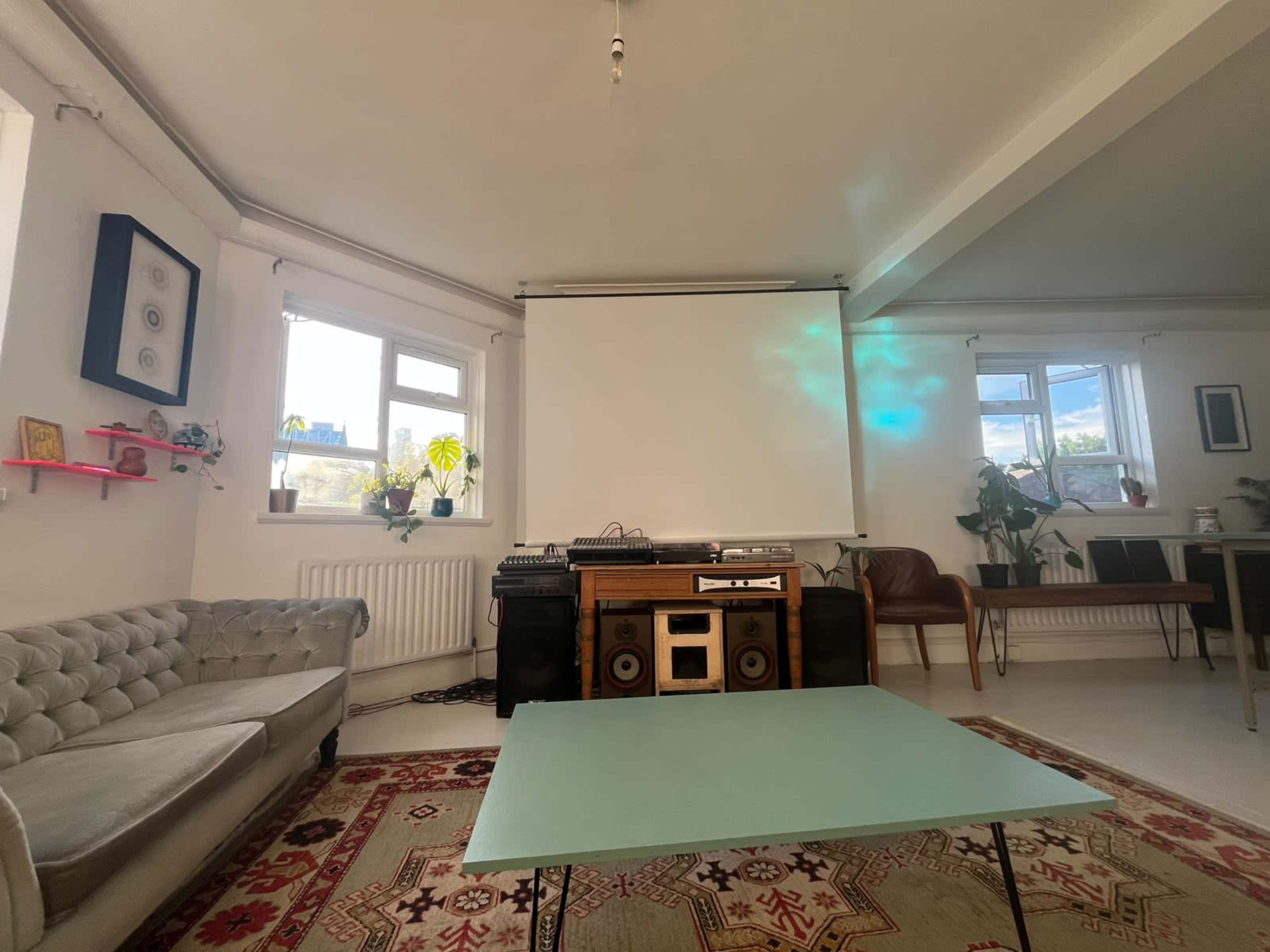 The image shows a bright room with a sofa, a retro audio setup, and a large projection screen on one wall.