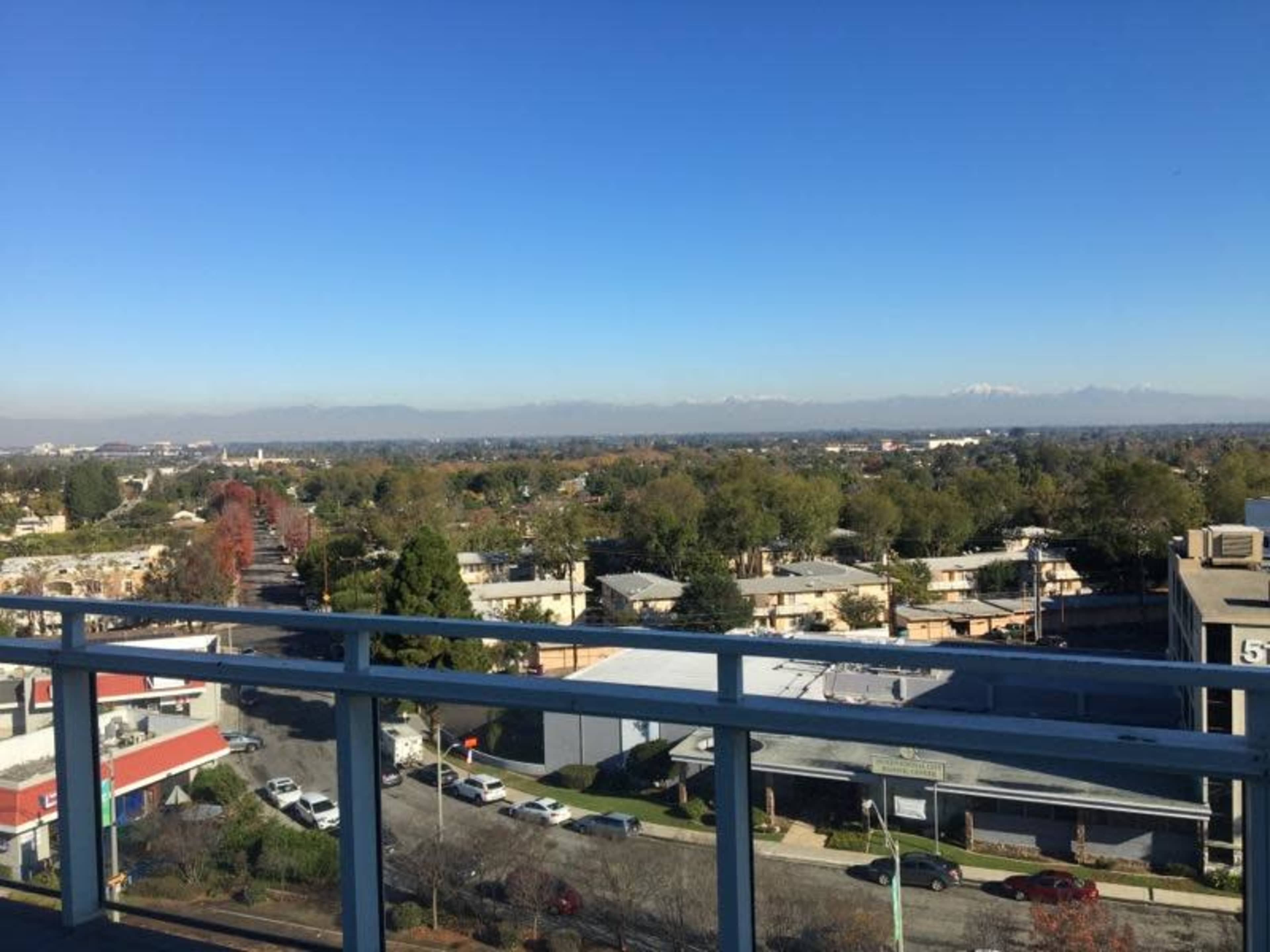 A panoramic view of a suburban area with buildings, trees, and distant mountains under a clear blue sky.