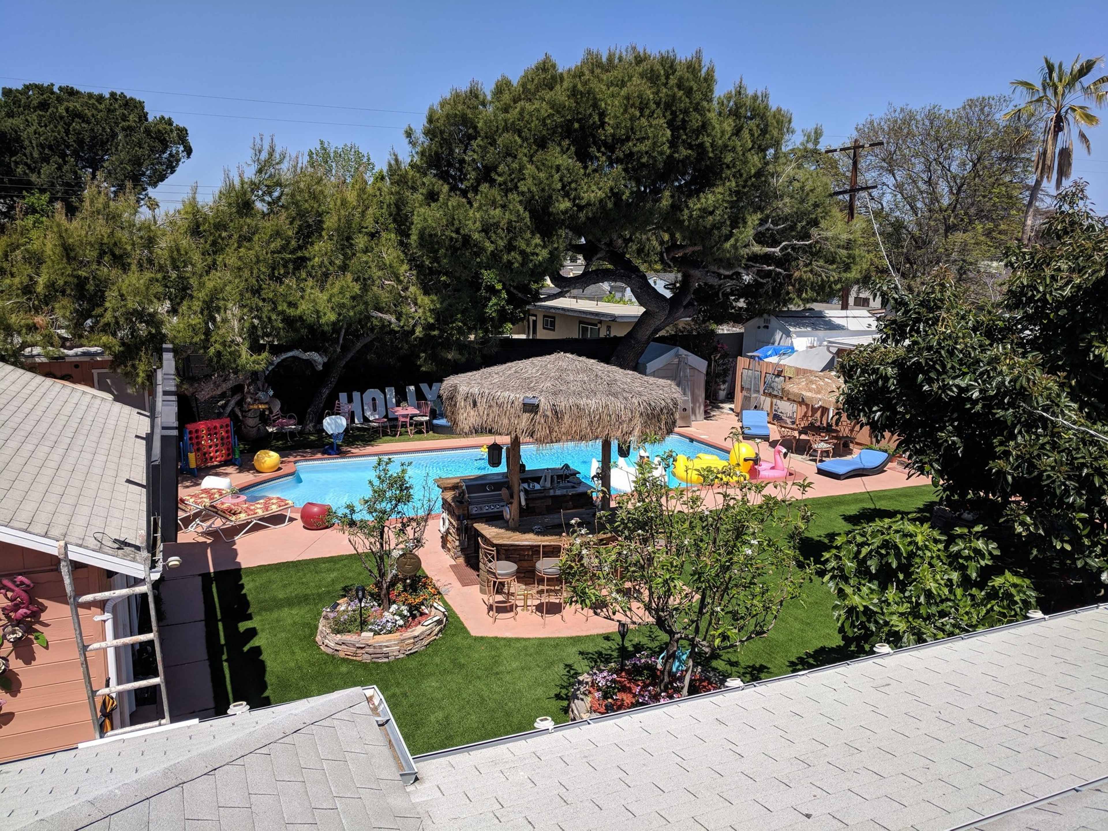 A backyard with a swimming pool, a thatched-roof gazebo, lounge chairs, and colorful inflatable items scattered around.