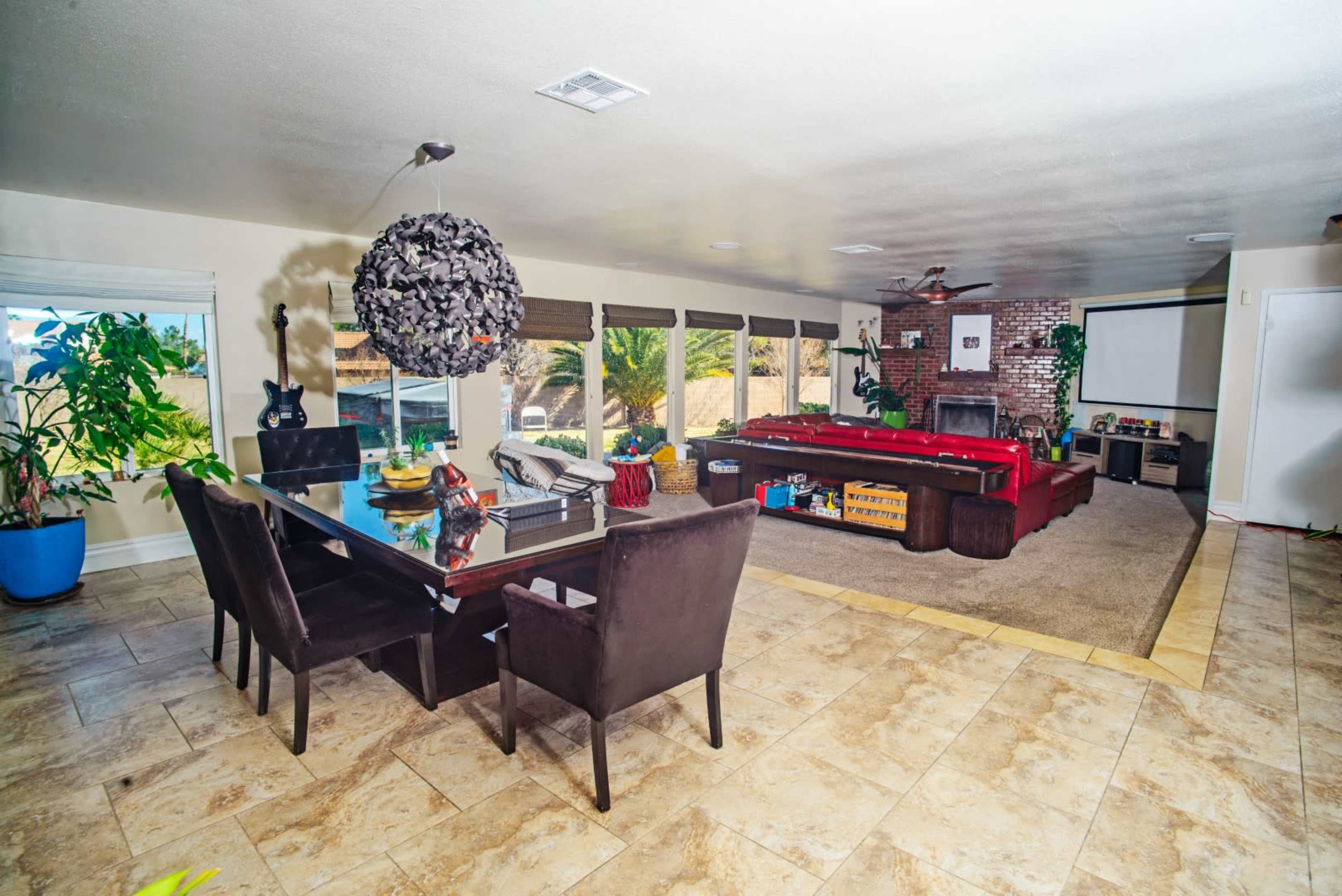A spacious living area features a dining table, a red sectional sofa, and a large window overlooking a garden.
