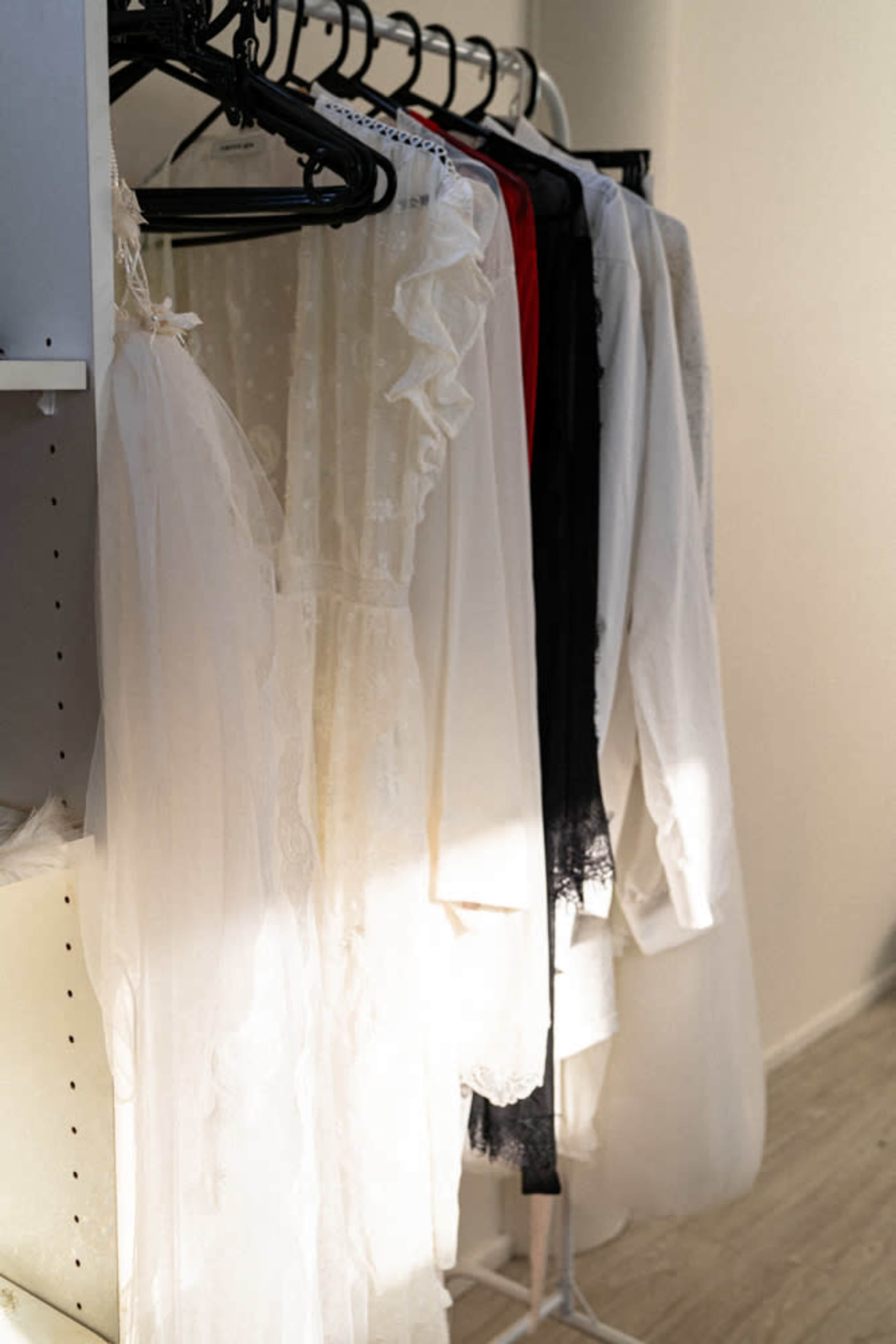 Several garments hang on black hangers, displaying a mix of white and black clothing in a well-lit room.
