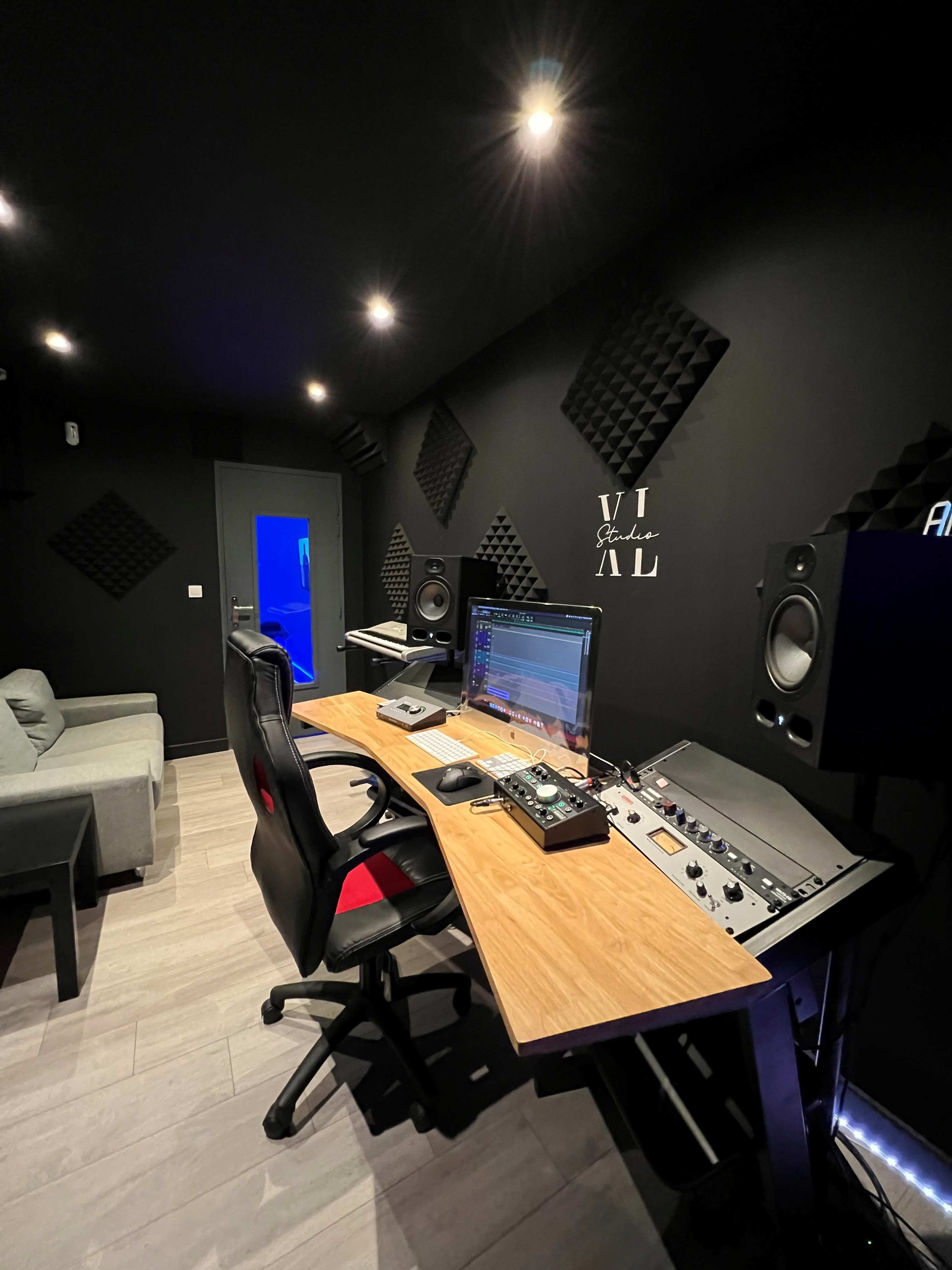 A modern recording studio with acoustic panels, a computer setup, and professional audio equipment.