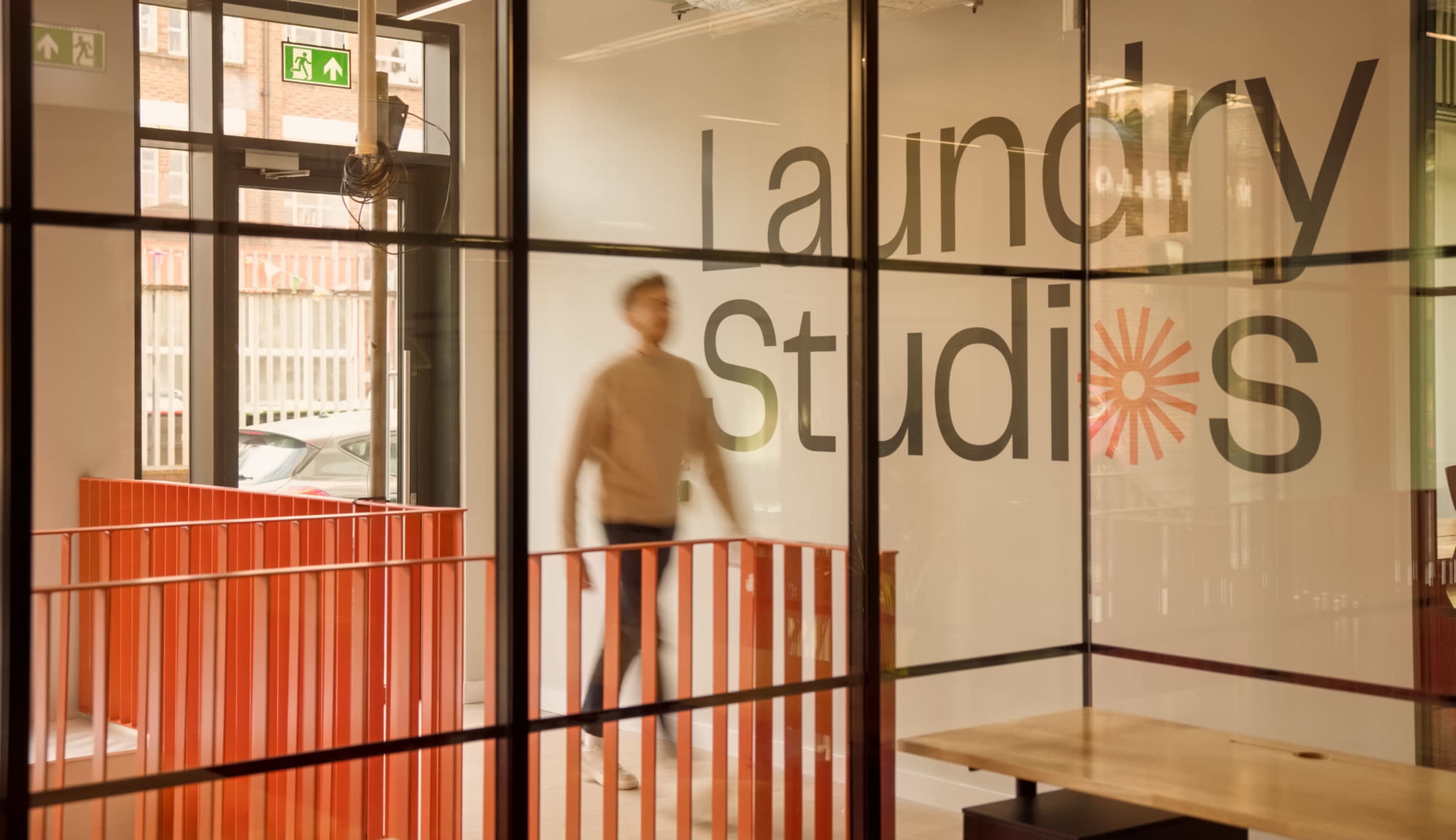 A person walks past a glass wall displaying the words "Laundry Studios" in a modern interior space.