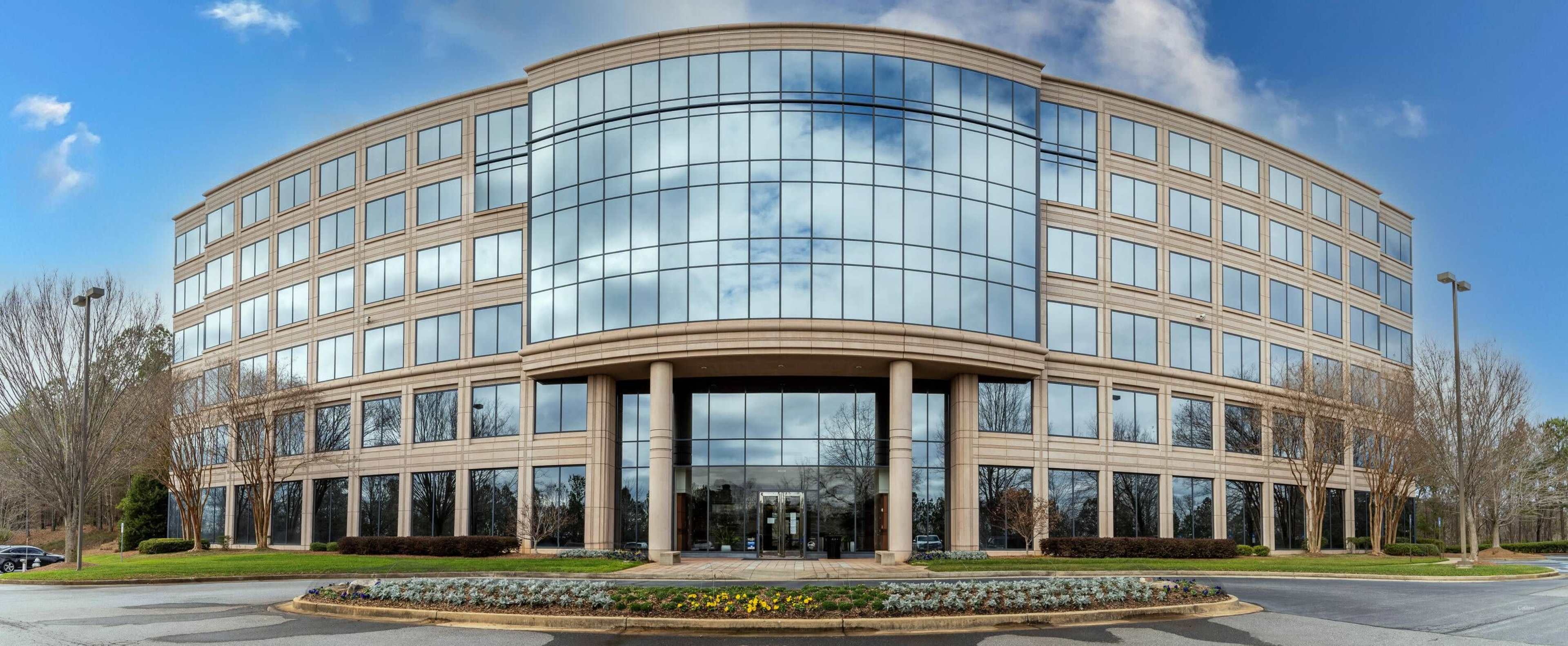 A modern office building with large glass windows and a curved facade is situated on a landscaped lot.