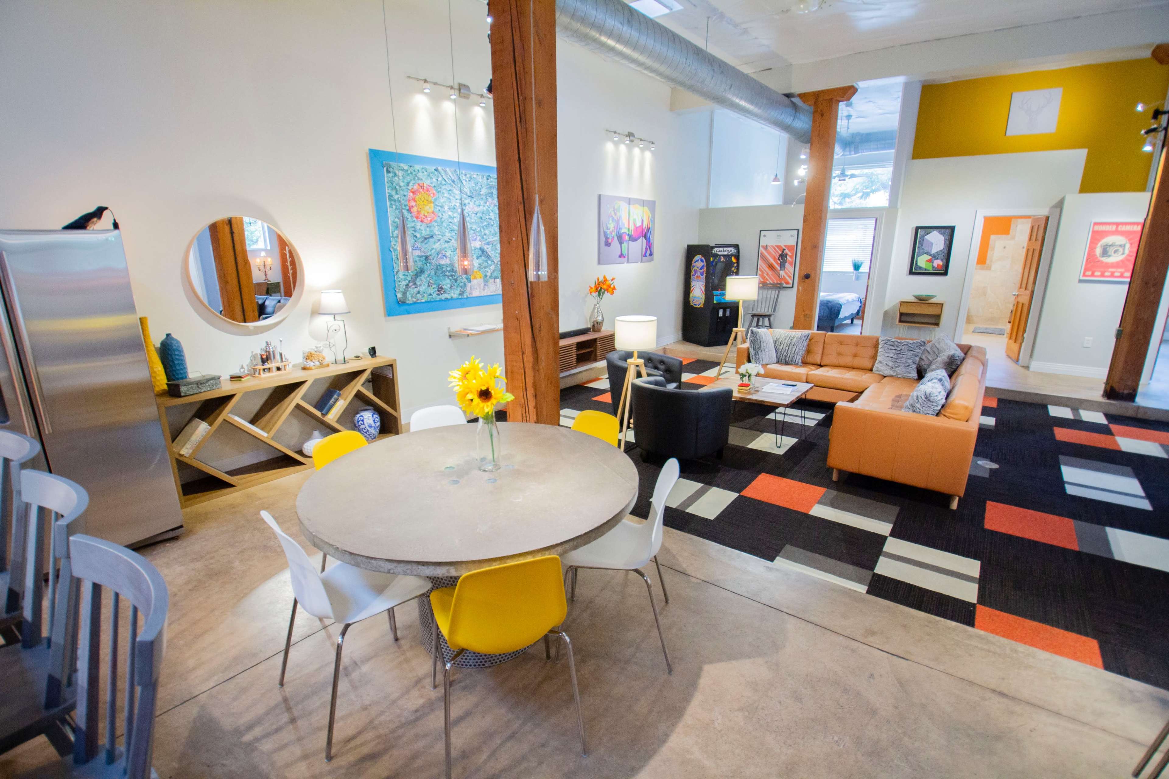 A spacious, modern living area featuring a circular dining table, an orange couch, and various artworks on the walls.