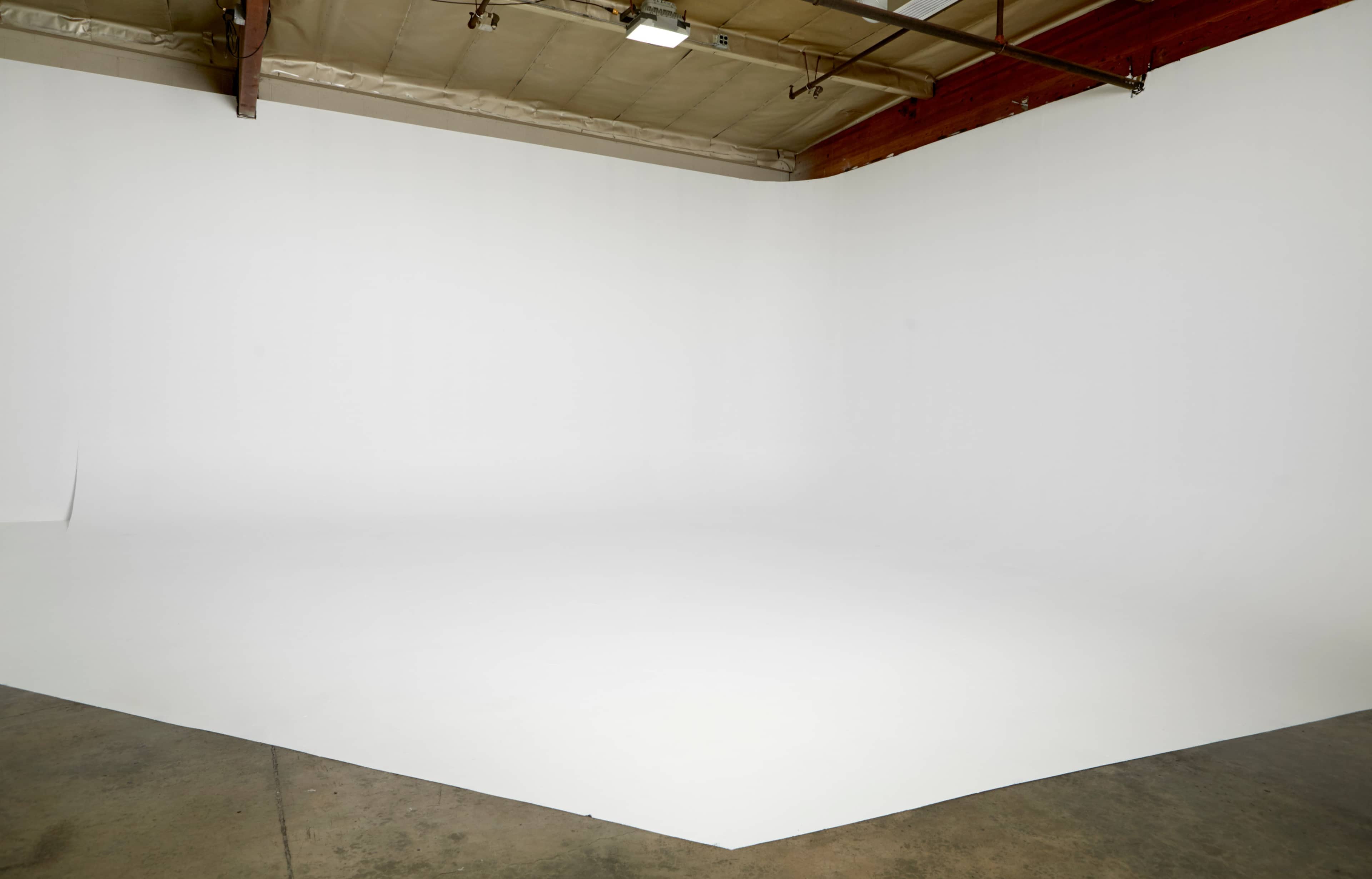 A large, empty photo studio with a white backdrop and concrete floor.