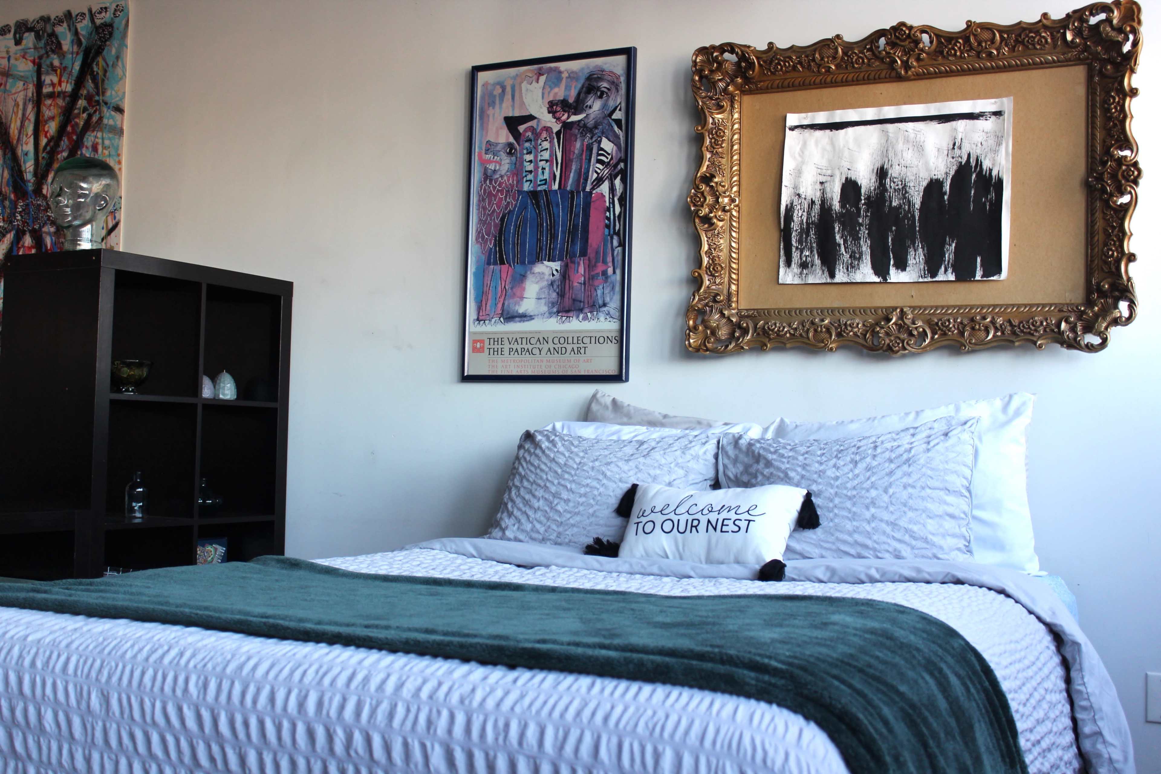 A neatly arranged bedroom features a bed with white bedding, a green throw blanket, a decorative pillow, and framed artwork on the walls.