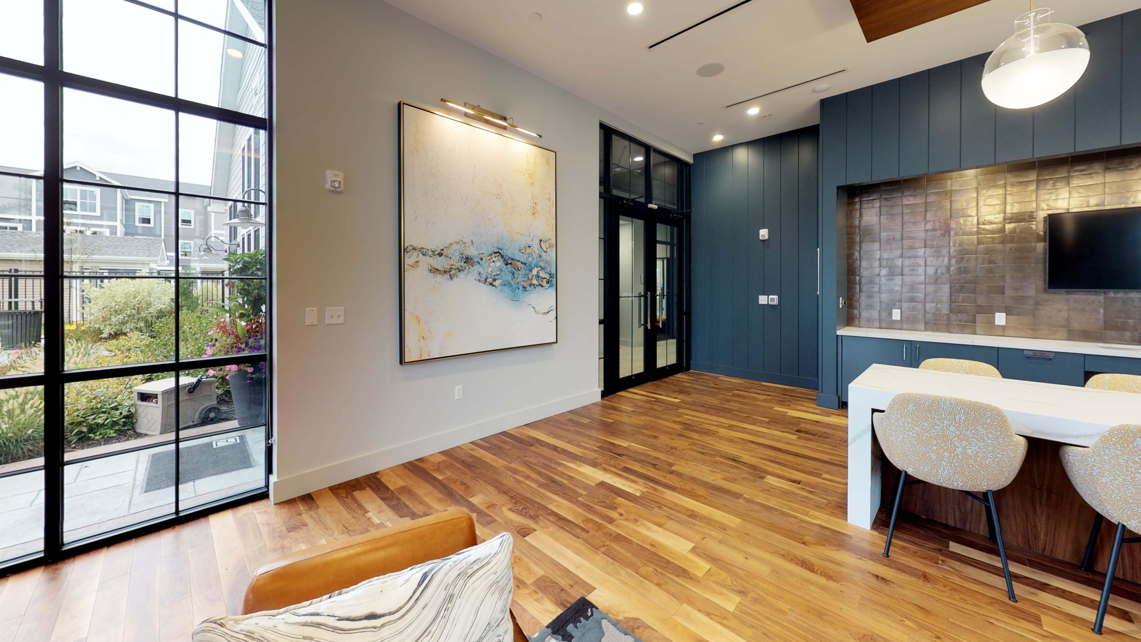 A modern interior space featuring a large painting on the wall, a dining area with a table and chairs, and large windows that overlook a garden.