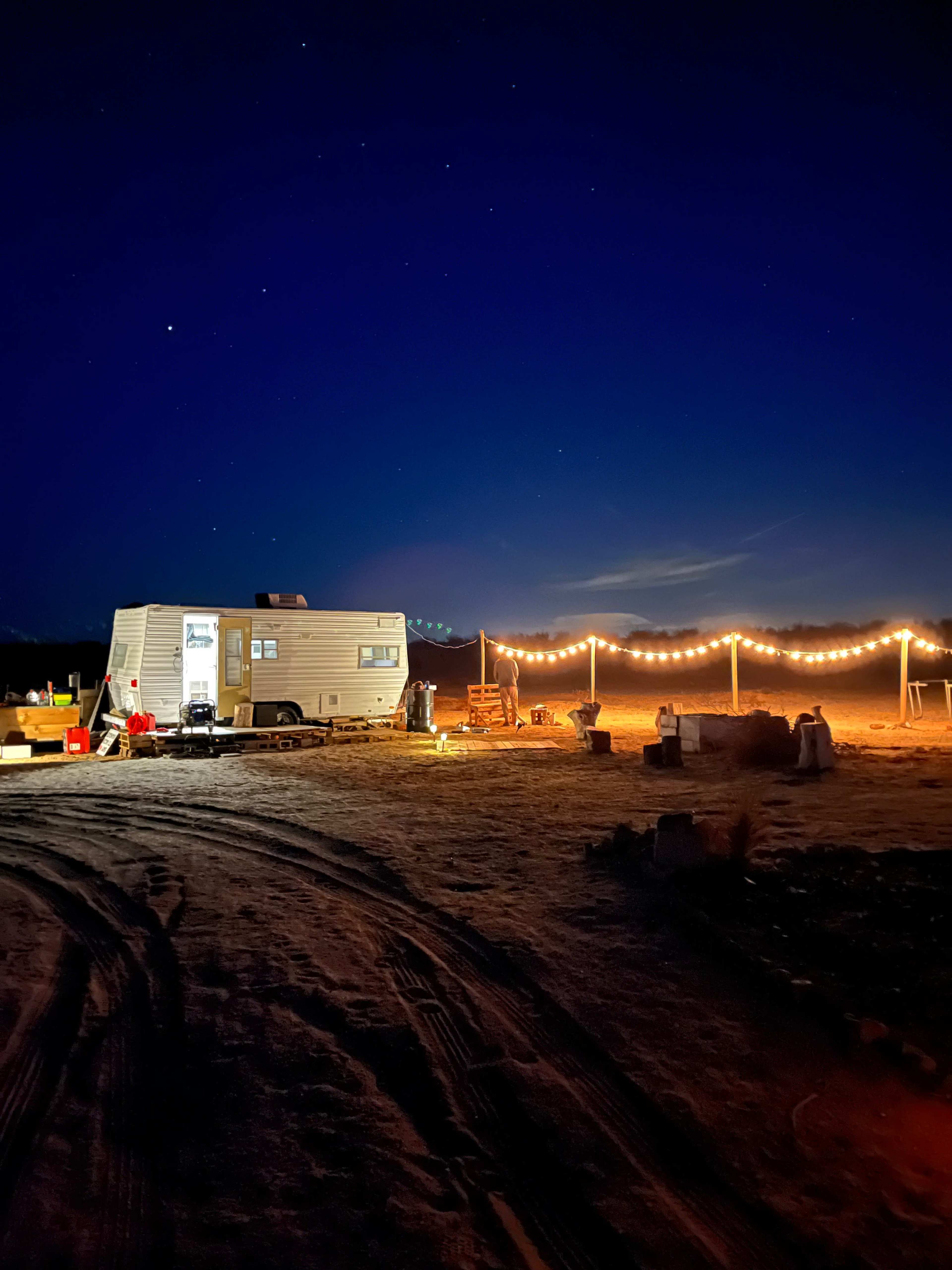A trailer is set up in a dark, open area, illuminated by string lights against a starry night sky.