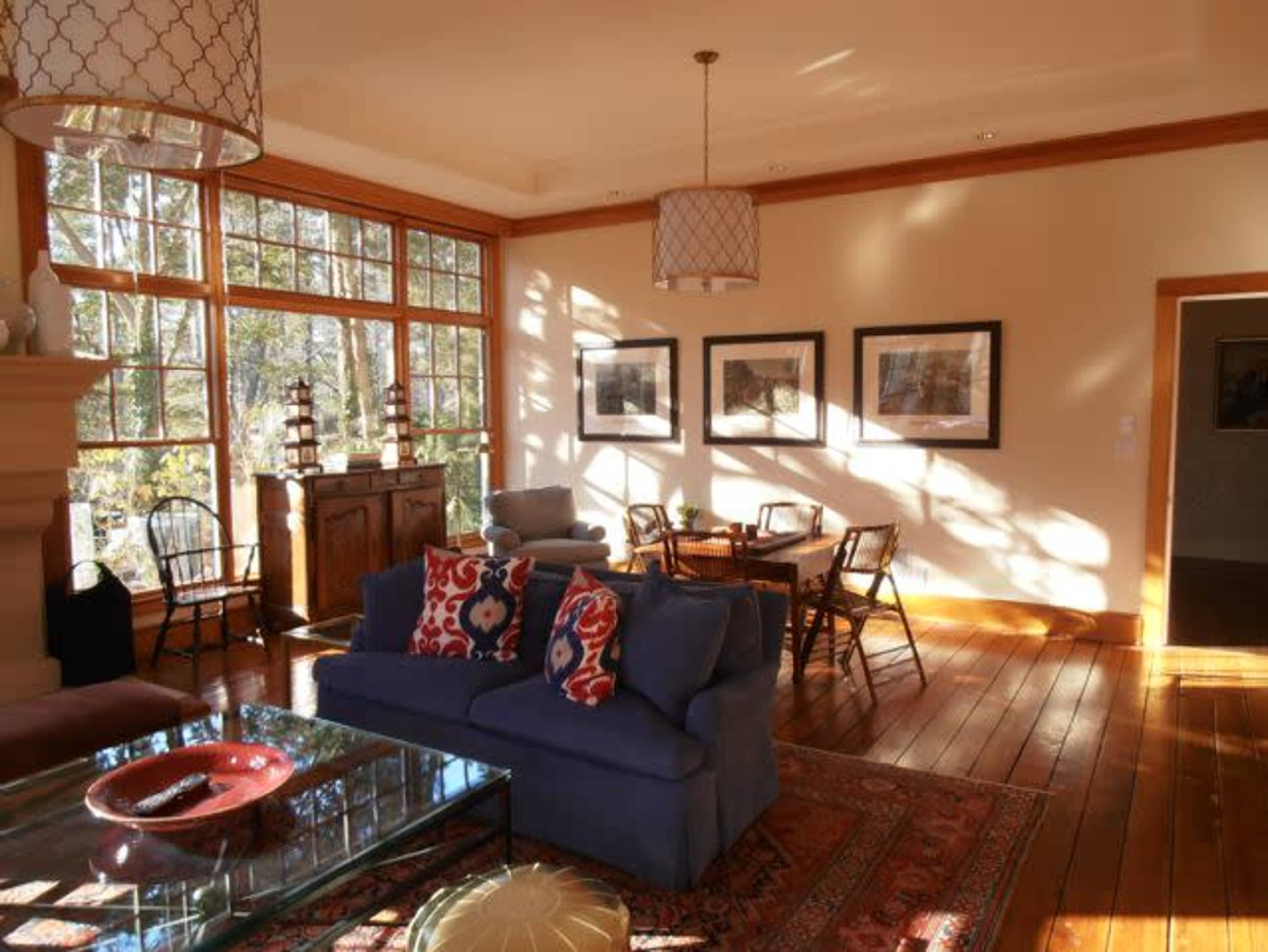 A cozy living room featuring a blue sofa, a wooden dining table with chairs, and large windows allowing natural light to fill the space.