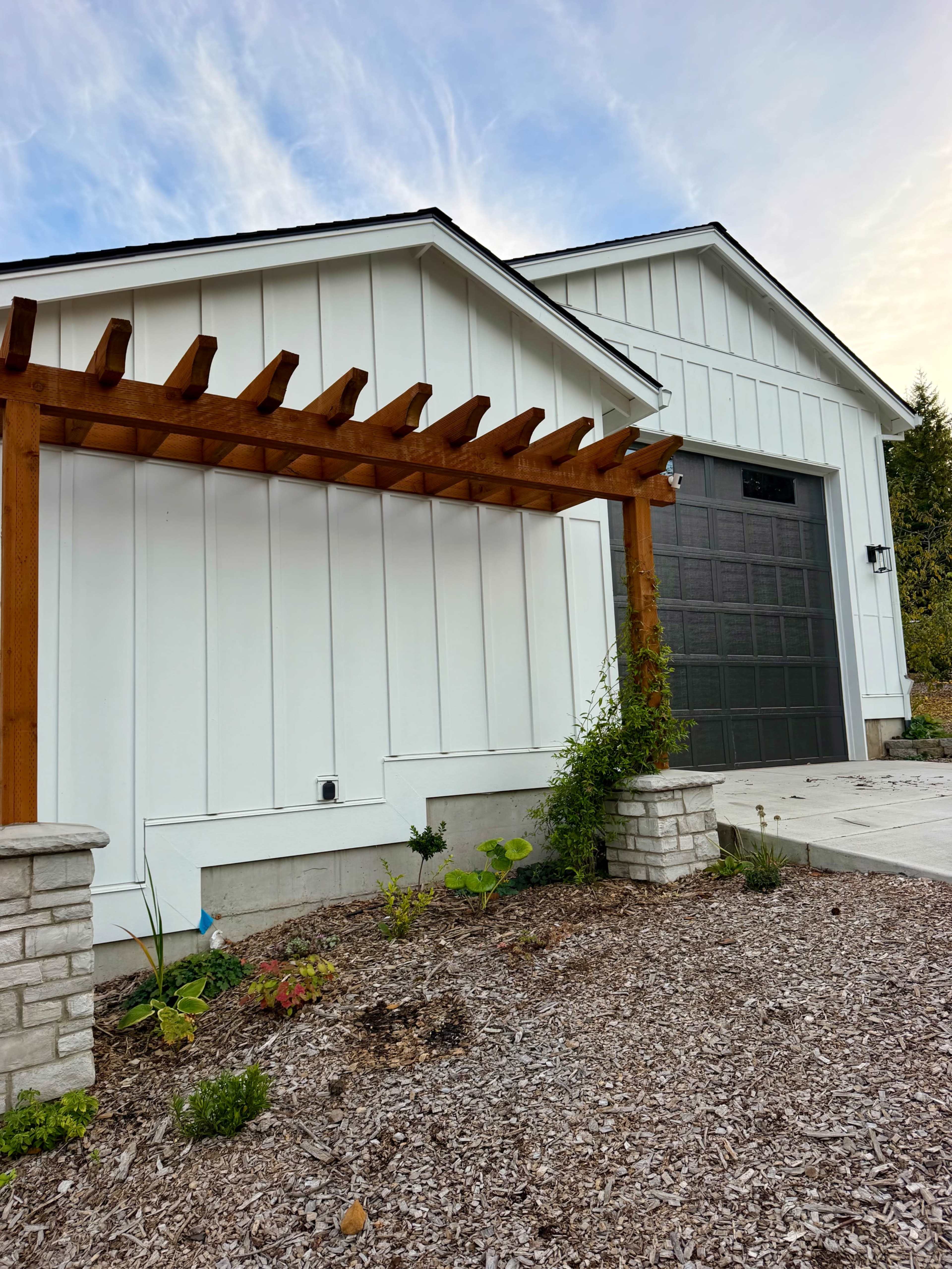 The image shows the exterior of a modern white house with a wooden pergola and a gray garage door.
