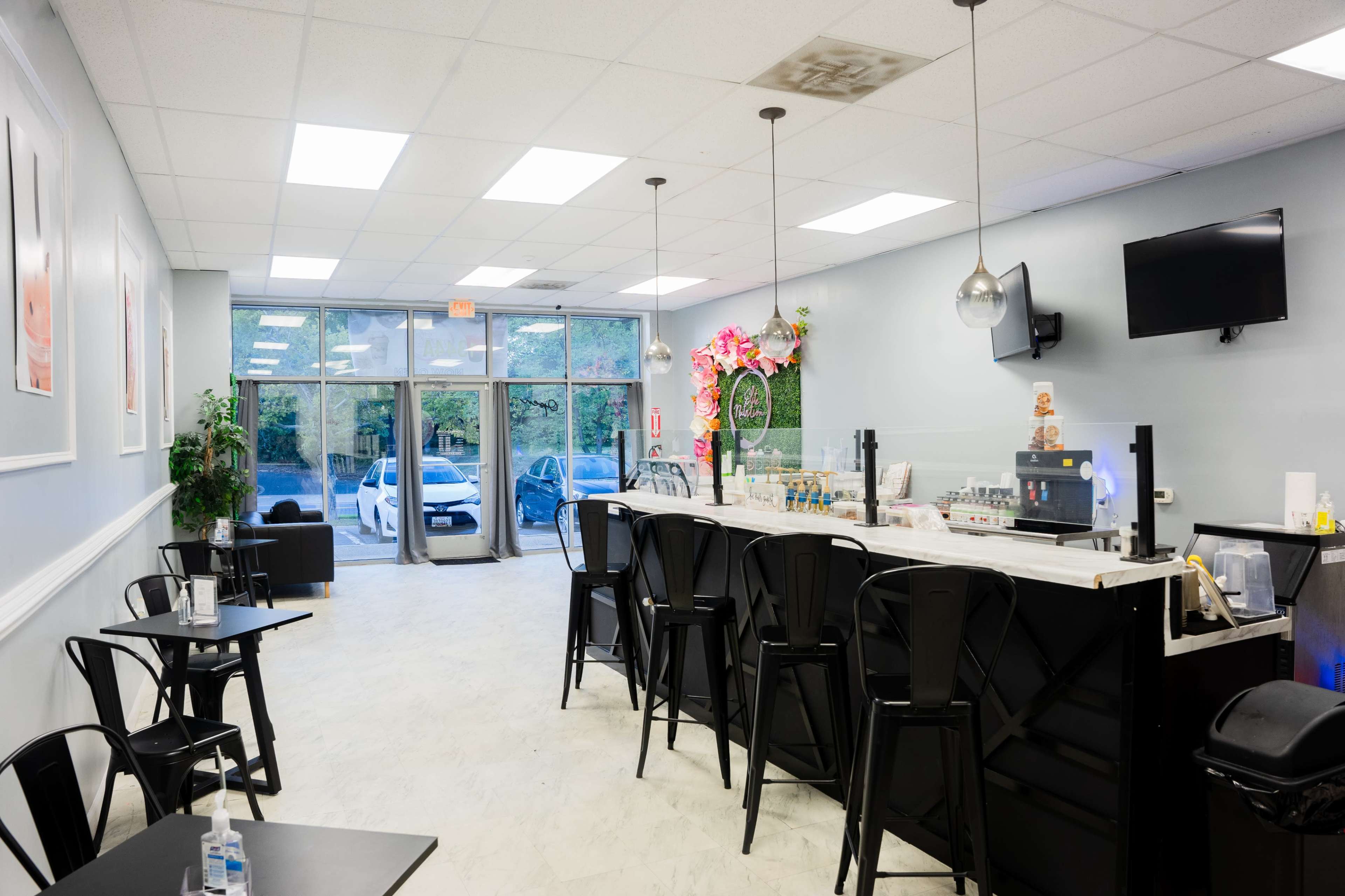 The image shows the interior of a modern café with a black bar counter, seating areas, and large windows facing an outdoor view.