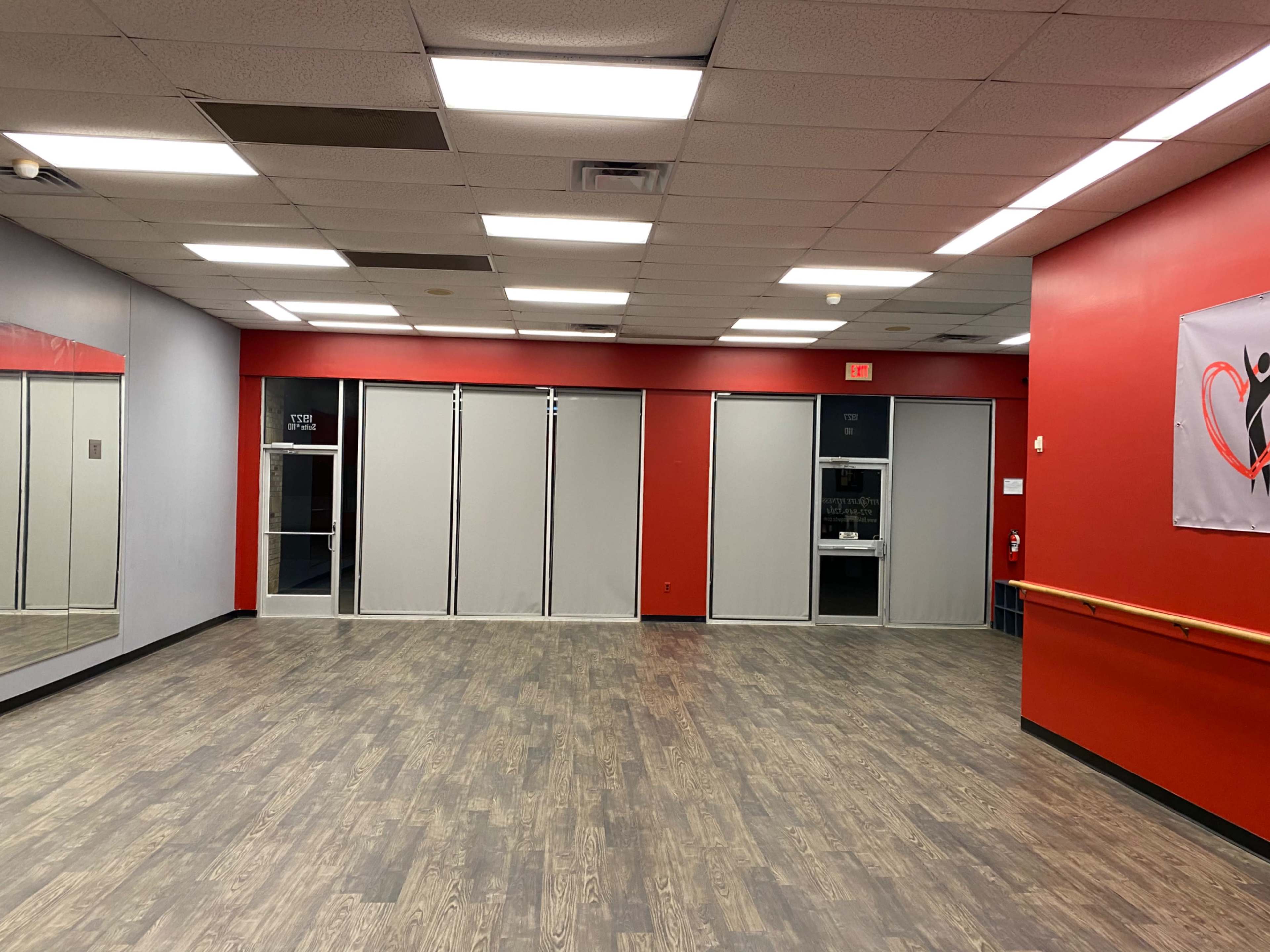 An empty studio space with hardwood floors, red walls, and a large mirror on one side.