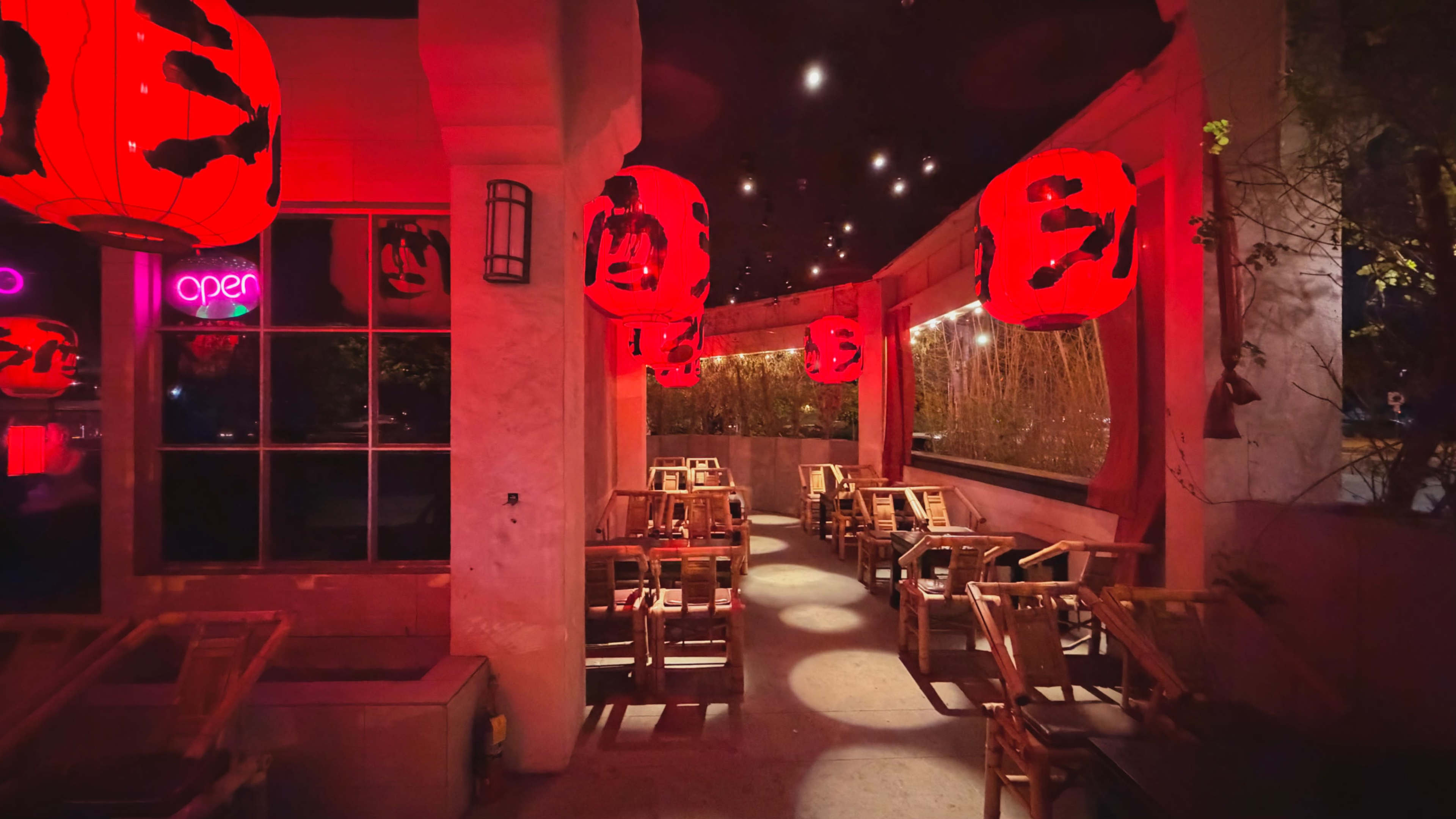 The image shows a dimly lit restaurant interior featuring red lanterns hanging from the ceiling and wooden tables arranged in the seating area.