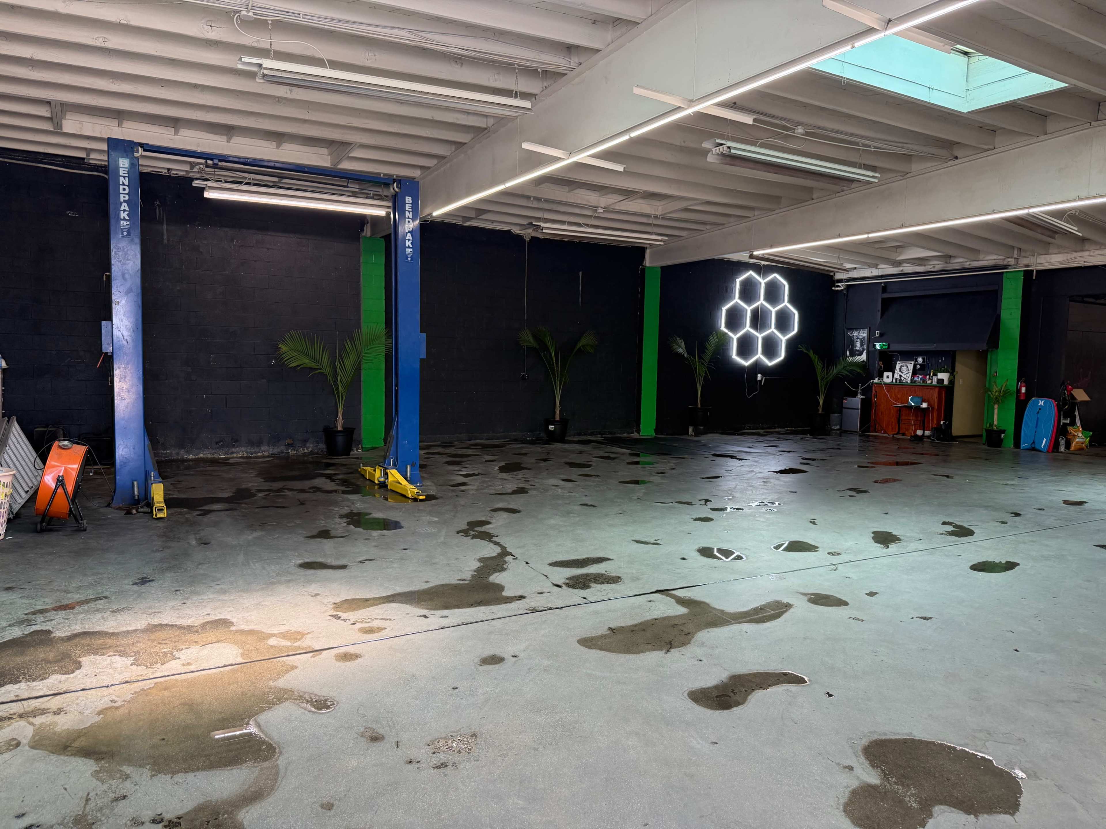 The image shows an empty garage space with two vehicle lifts, green and blue columns, and water stains on the concrete floor.