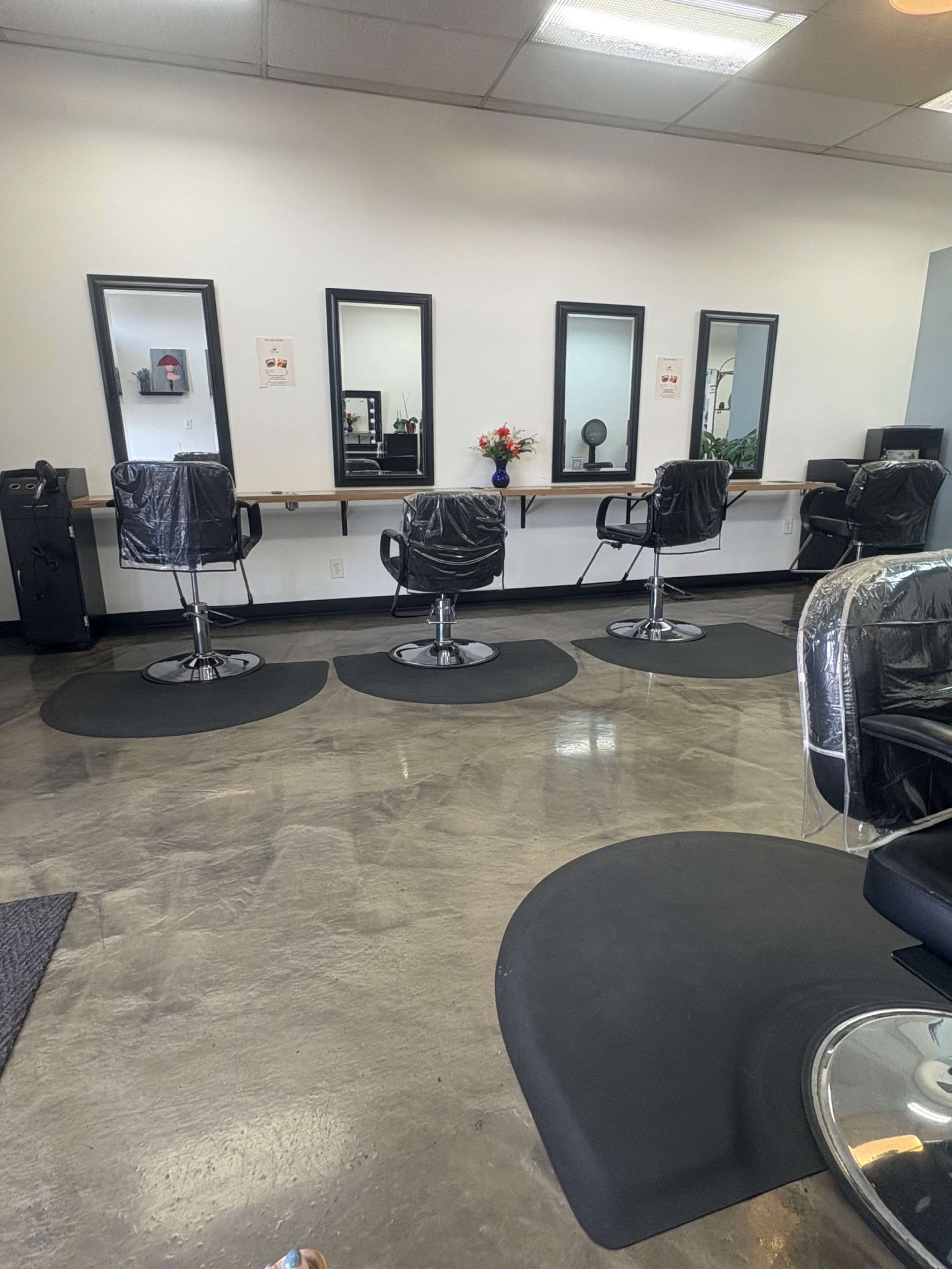 The image shows a spacious hair salon with three styling chairs in front of mirrors and a floral arrangement on a shelf.