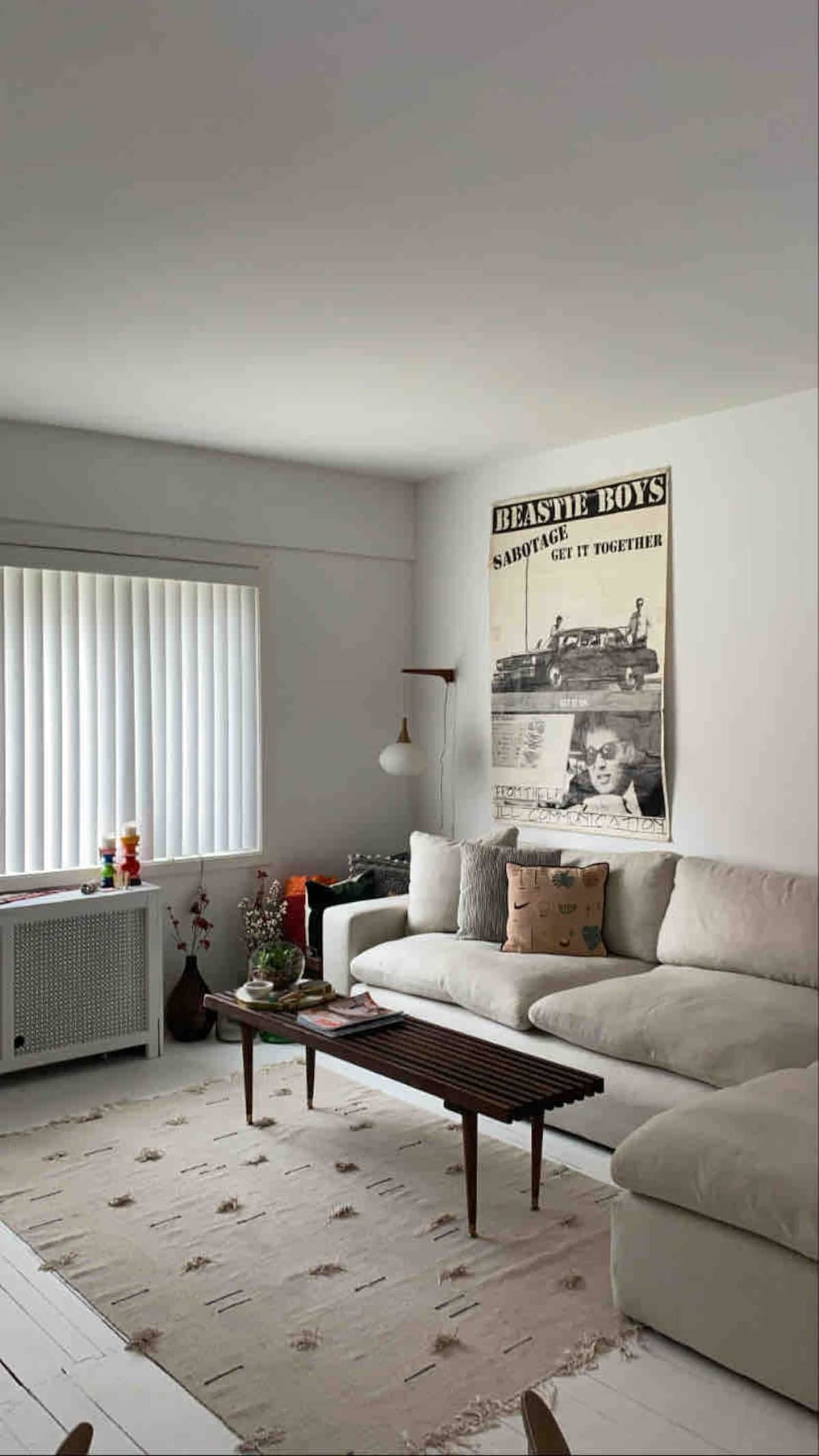 A modern living room featuring a light-colored sectional sofa, a wooden coffee table, and a large poster of the Beastie Boys on the wall.