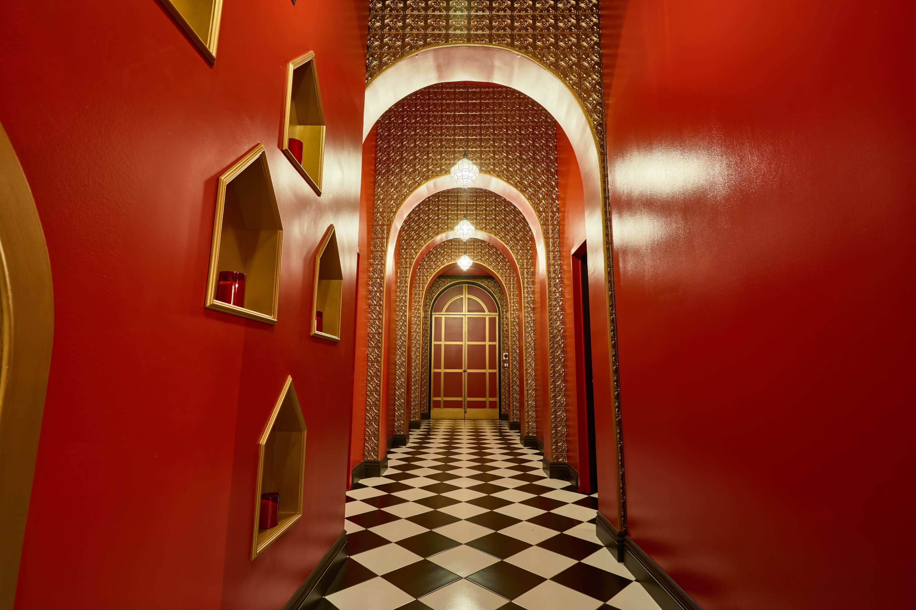 The image features a narrow corridor with red walls, decorative arches, and a black-and-white checkered floor.