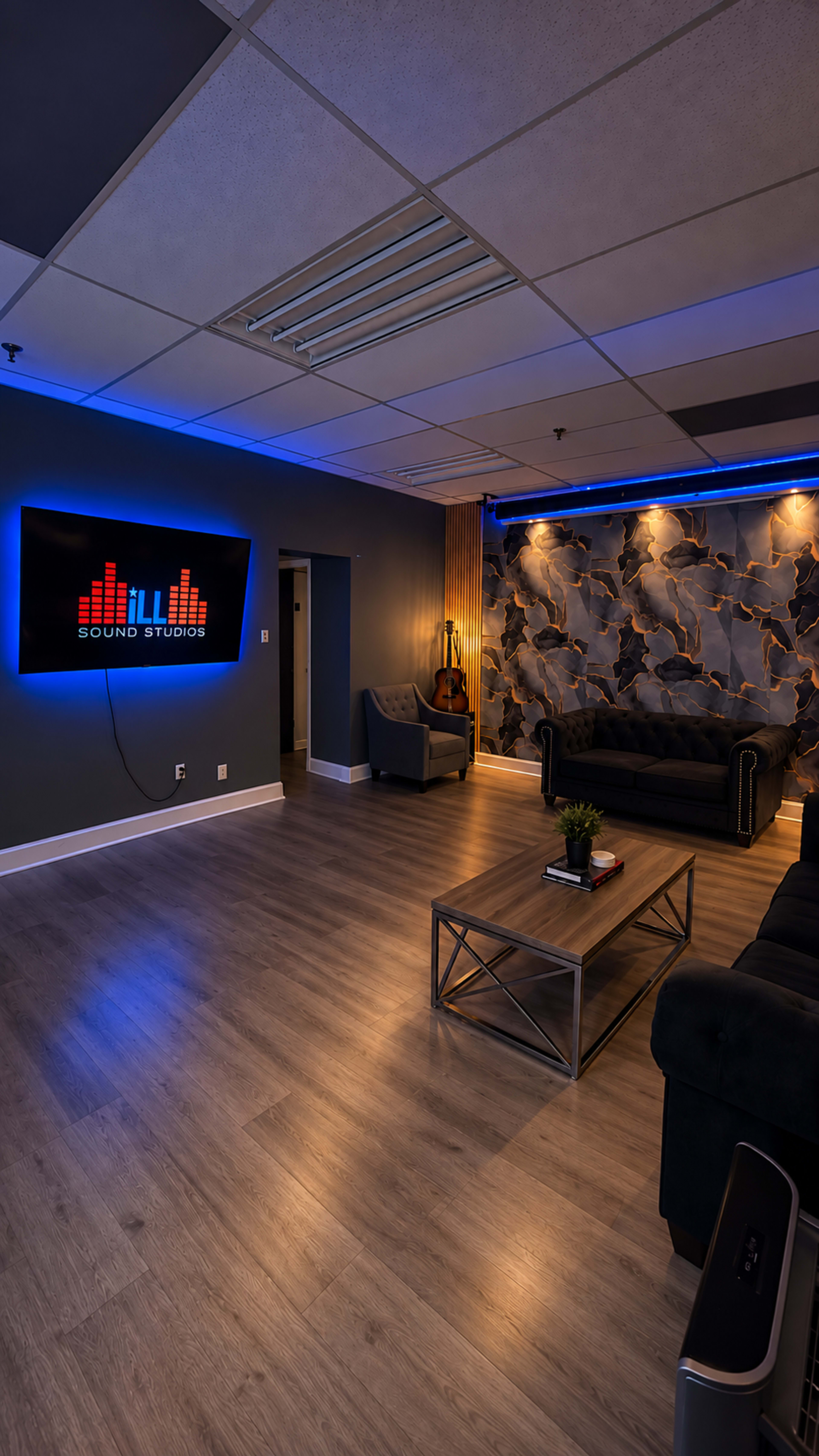 The image shows a modern sound studio lounge with a dark blue wall, a large screen displaying the studio's logo, a sleek coffee table, and a comfortable seating area.