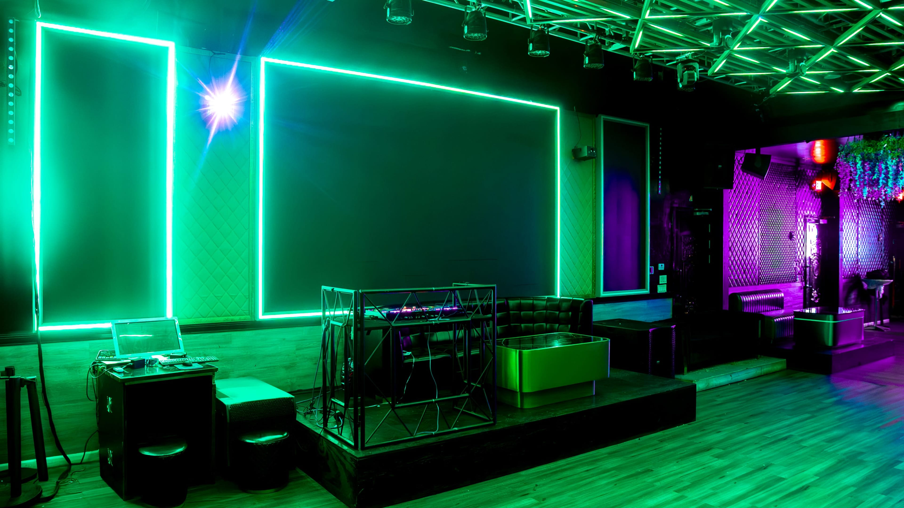 The image shows a dimly lit club interior with neon green and purple lighting, featuring a DJ booth and lounge seating against a modern decor backdrop.