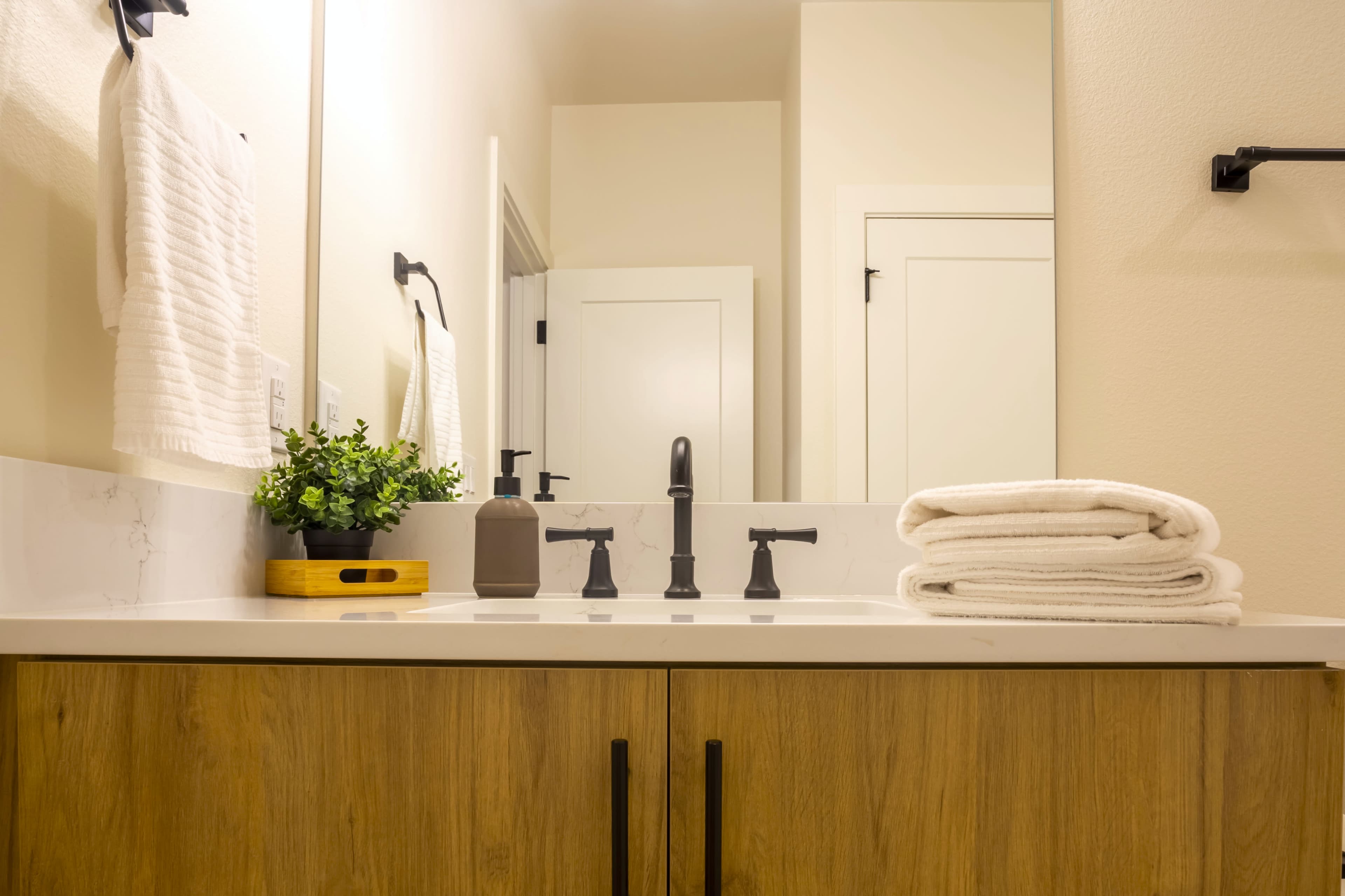 The image shows a bathroom countertop with neatly stacked white towels, a small potted plant, and modern faucet fixtures.