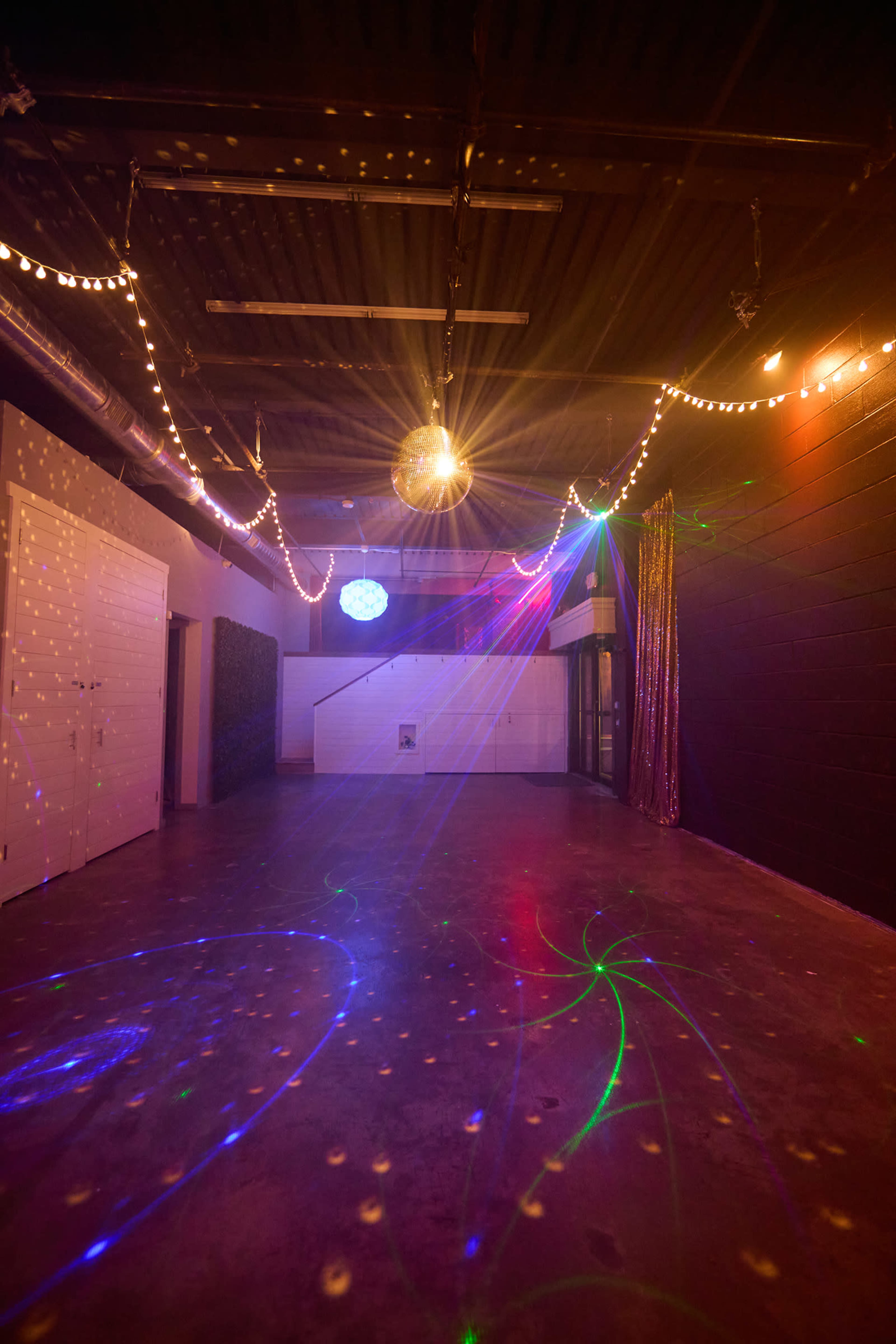The image shows an empty room with string lights and a disco ball, casting colorful patterns on the floor.