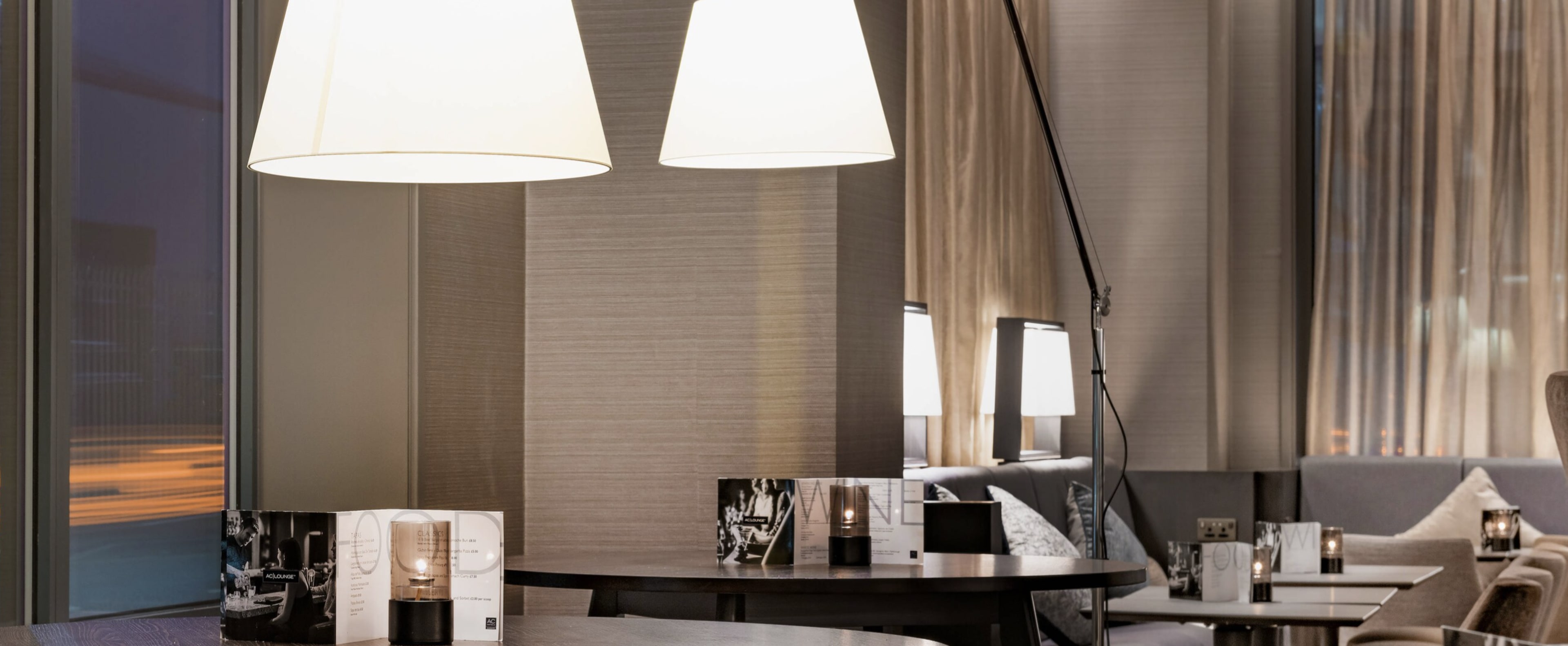 A modern interior of a lounge with two large pendant lamps hanging above a set of tables adorned with candles and decorative items.