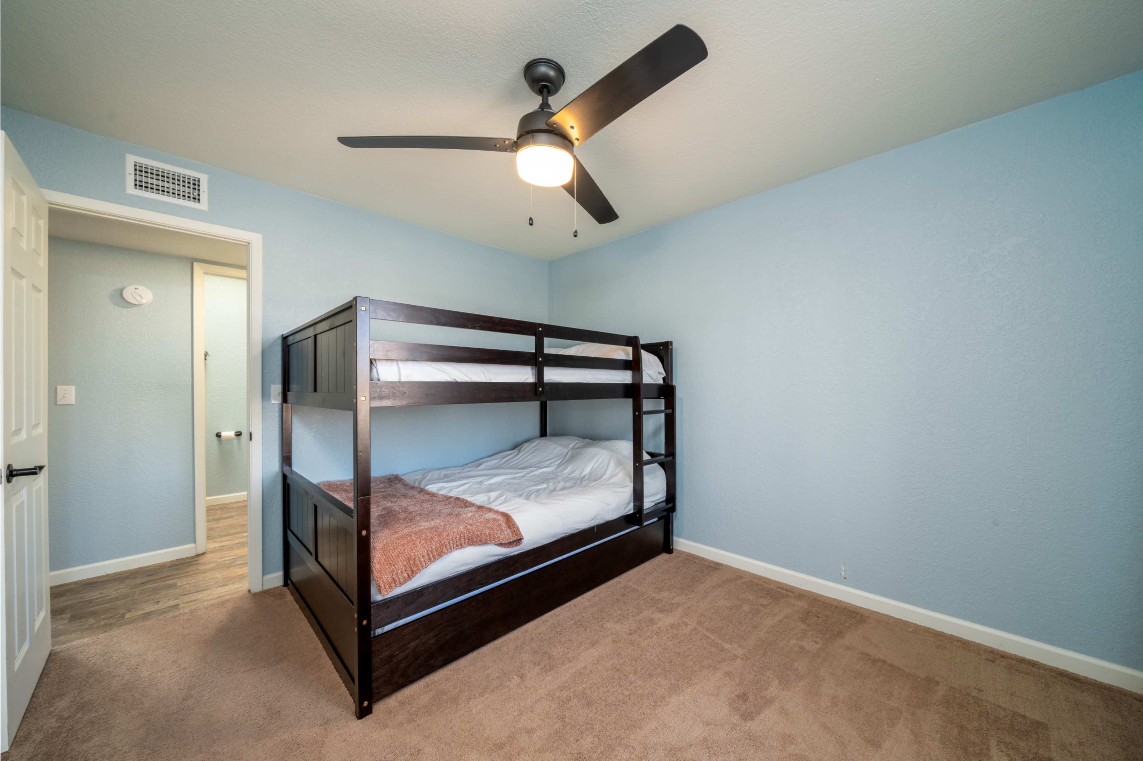 The image shows a bedroom with a bunk bed, a ceiling fan, and light blue walls.