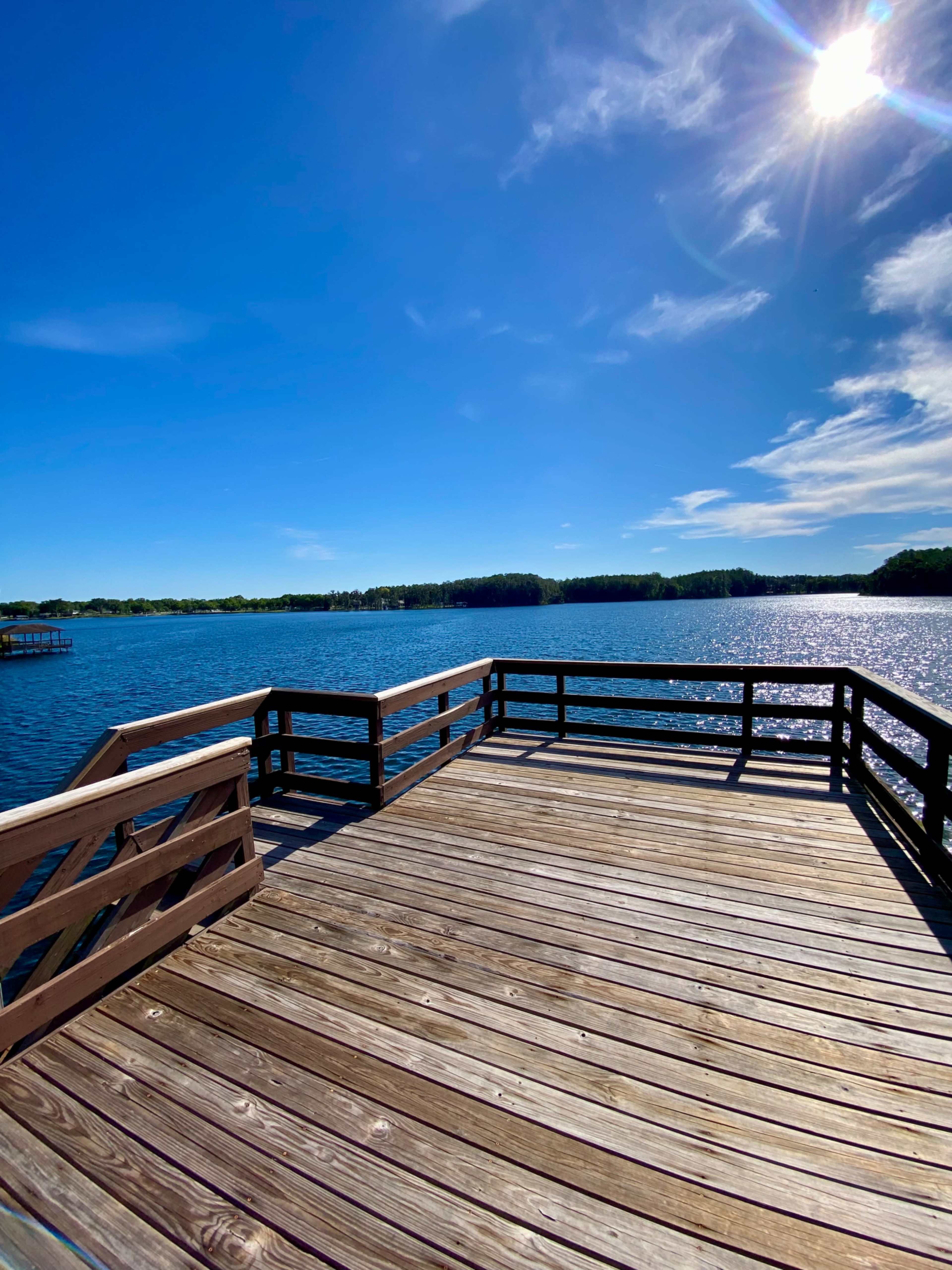 A wooden dock extends over a calm lake under a clear blue sky.