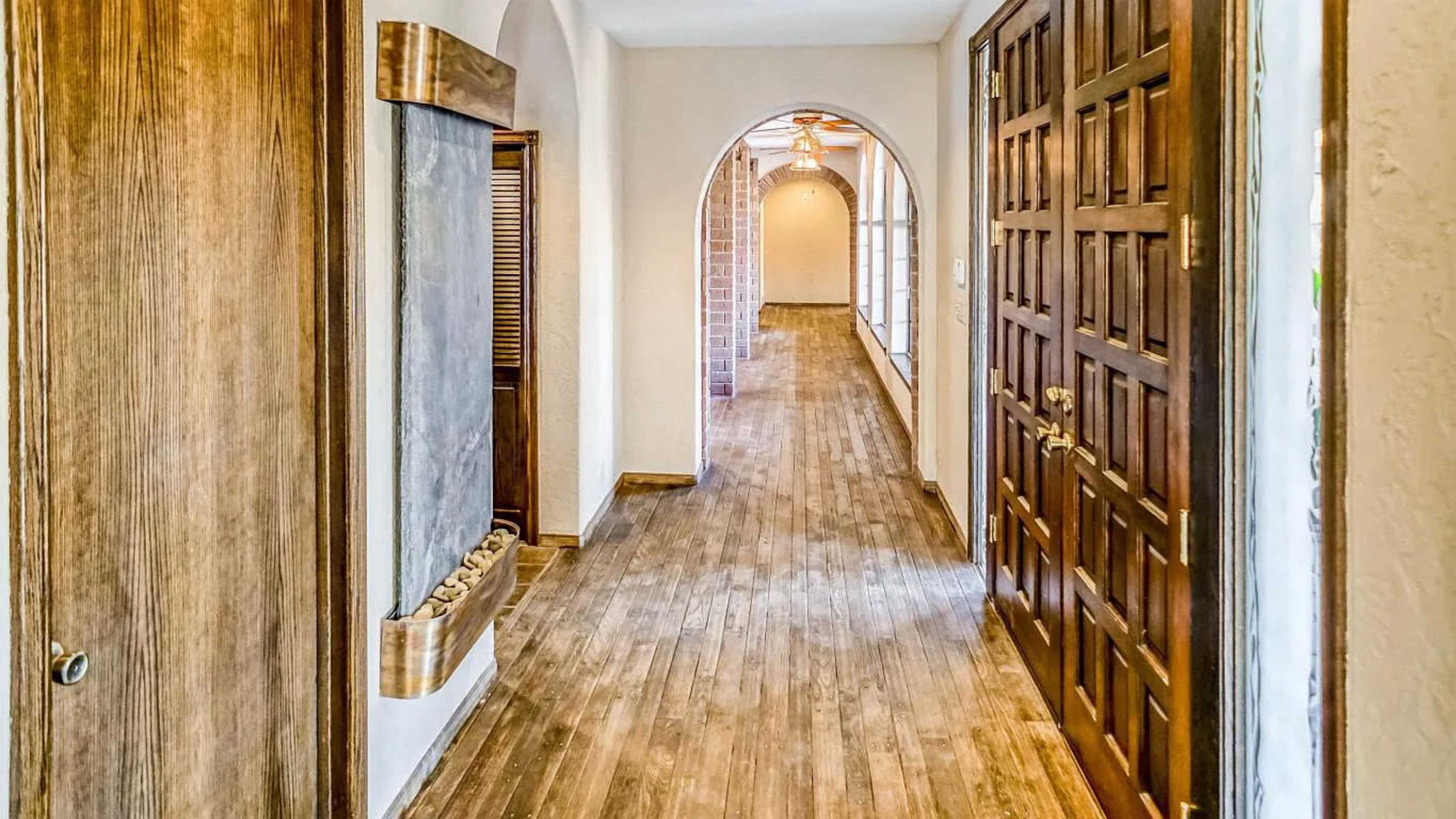 A hallway features wooden floors and arched doorways leading to a brightly lit area.