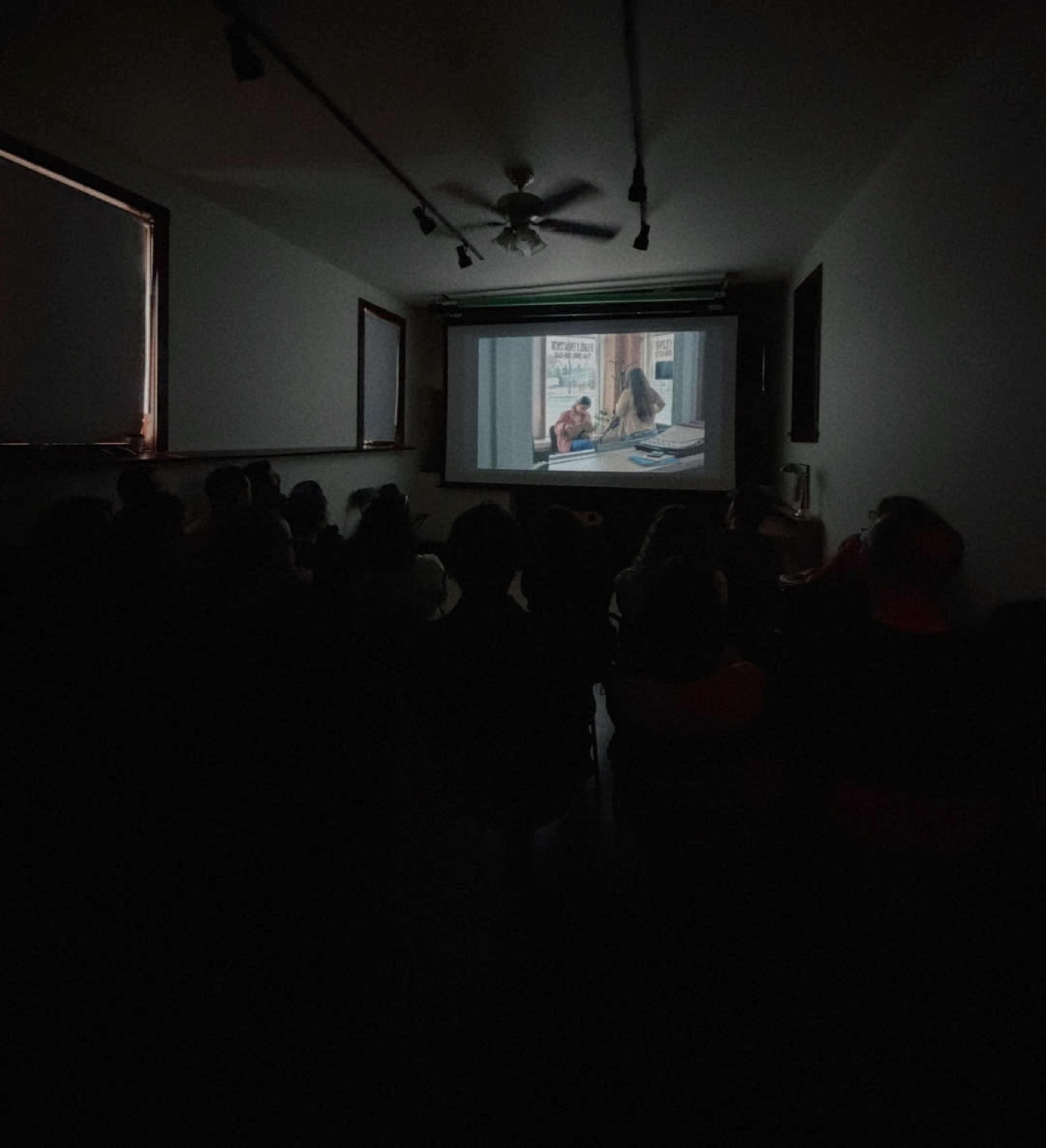 A group of people watches a film in a dimly lit room with a large screen displaying a scene.