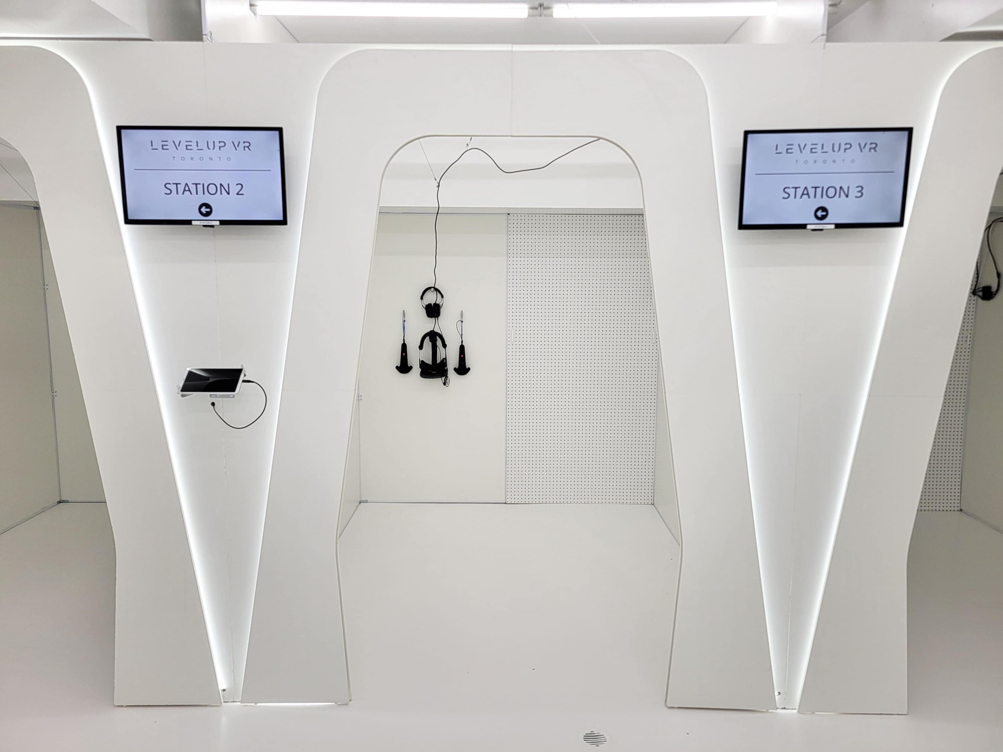 The image shows a modern VR gaming setup featuring two stations, each labeled and equipped with screens and virtual reality headsets.