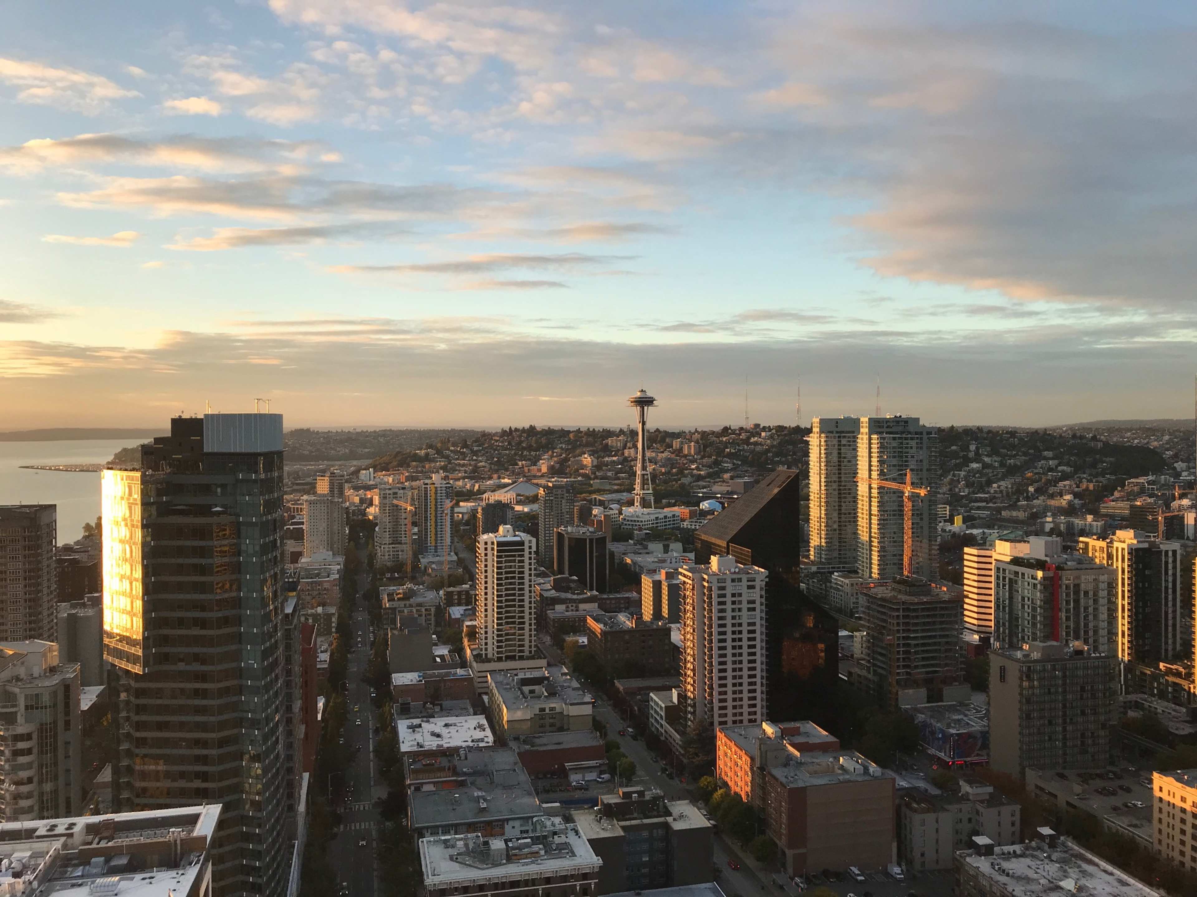 The image shows an aerial view of a city skyline at sunset, highlighting a mix of modern buildings and the Space Needle in the distance.