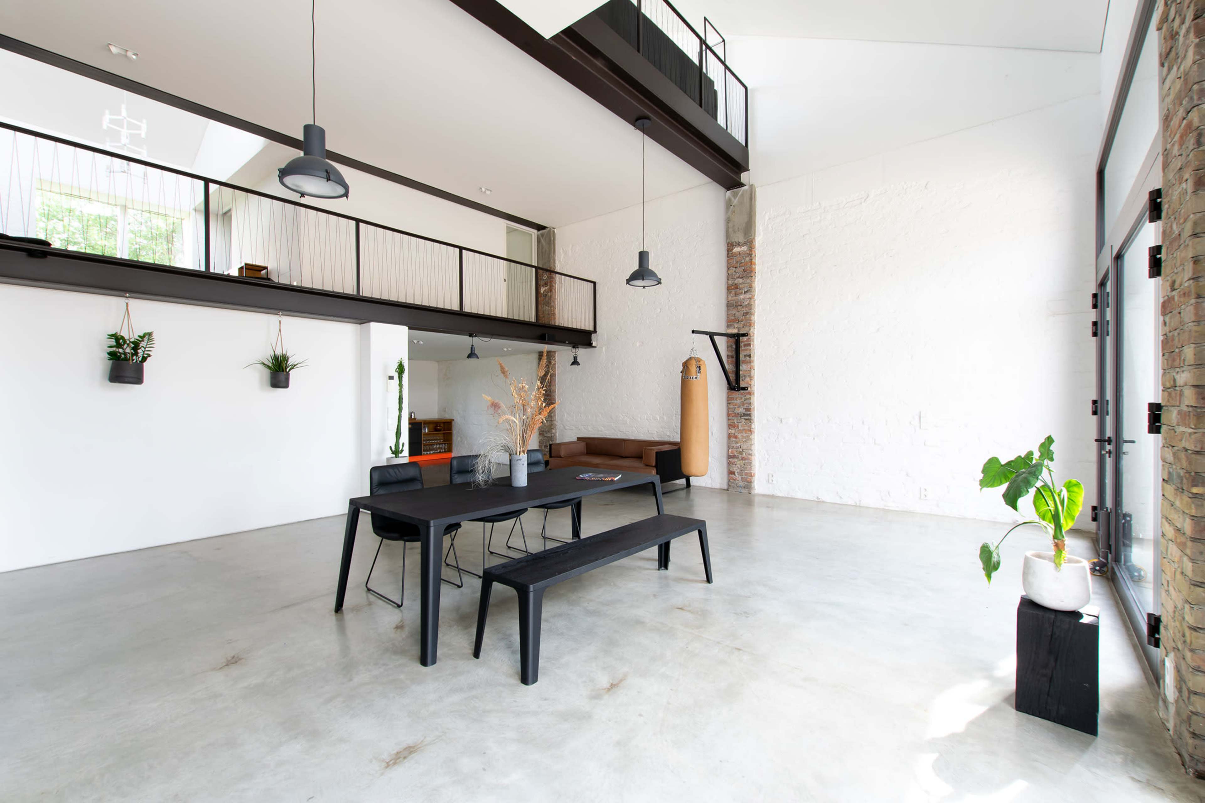 A modern industrial-style interior featuring a dining table with benches, high ceilings, and a mix of wooden and concrete elements.