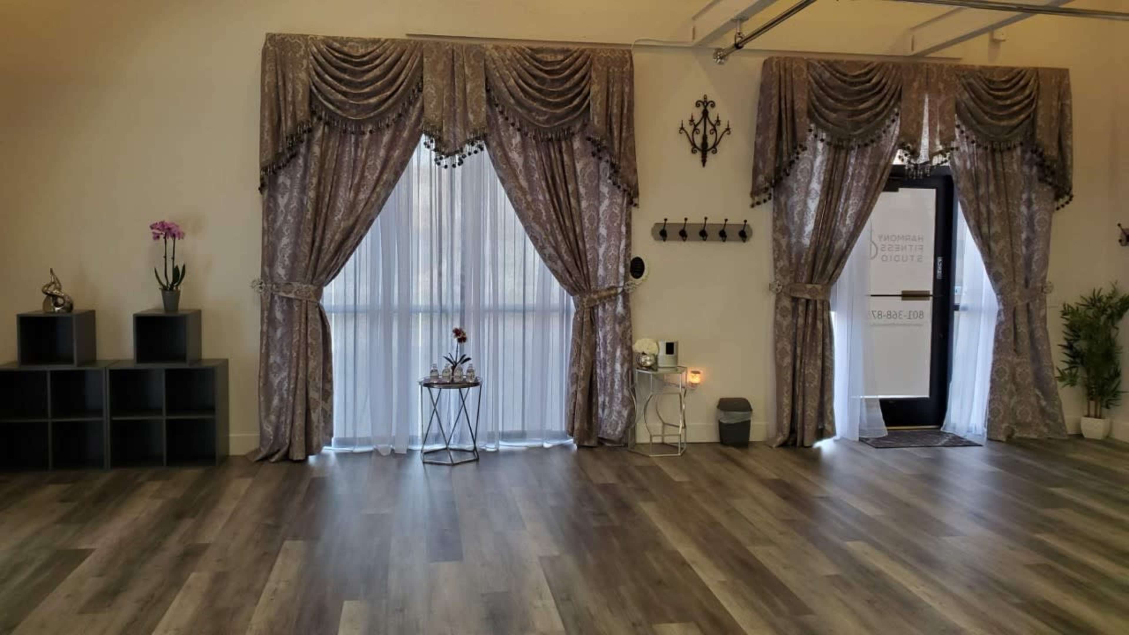 A spacious room with large windows covered by elegant curtains, a small table with a decorative plant, and a door leading outside.