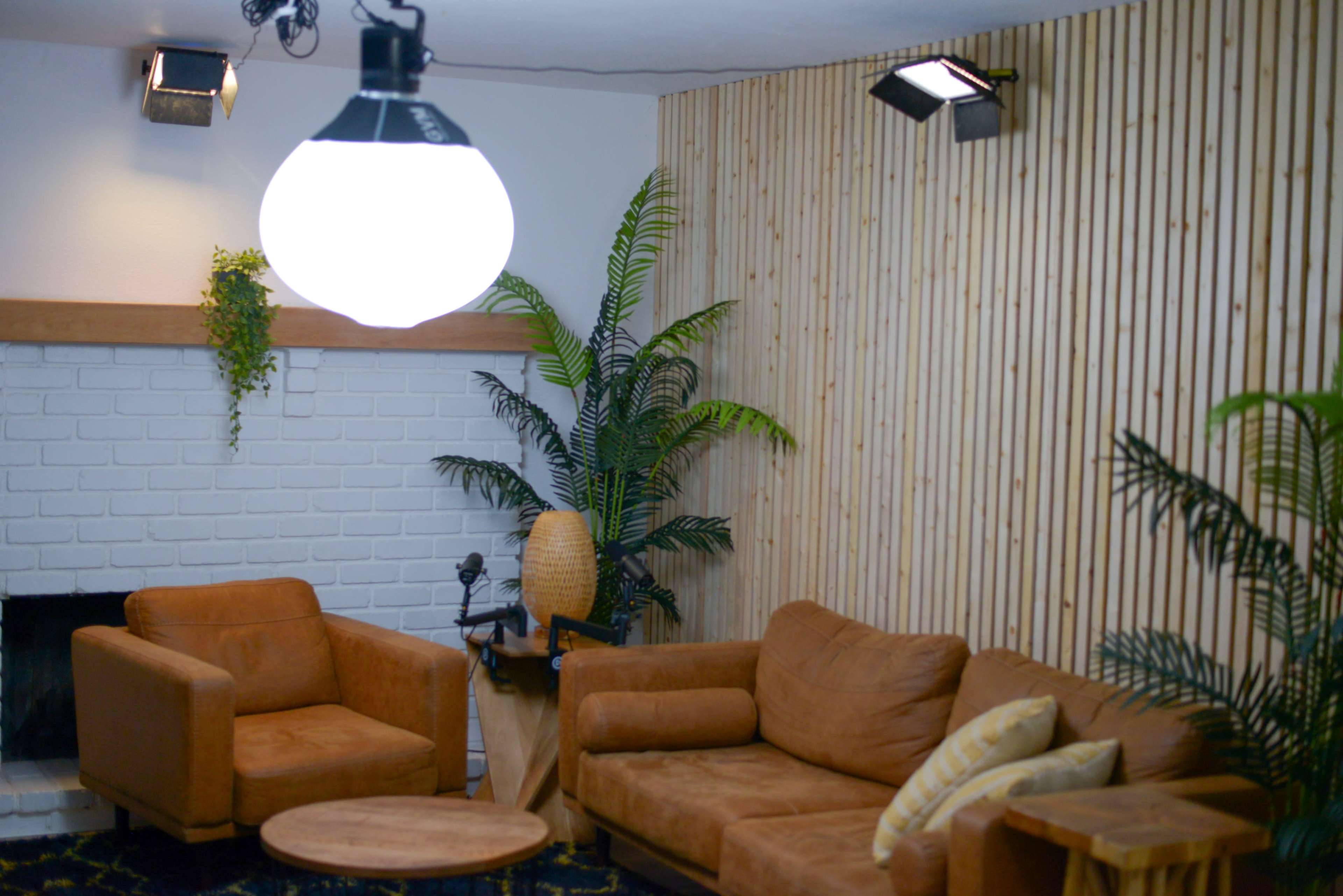 A cozy living room with a light fixture, two brown sofas, a round coffee table, and plants against a wooden-paneled wall.