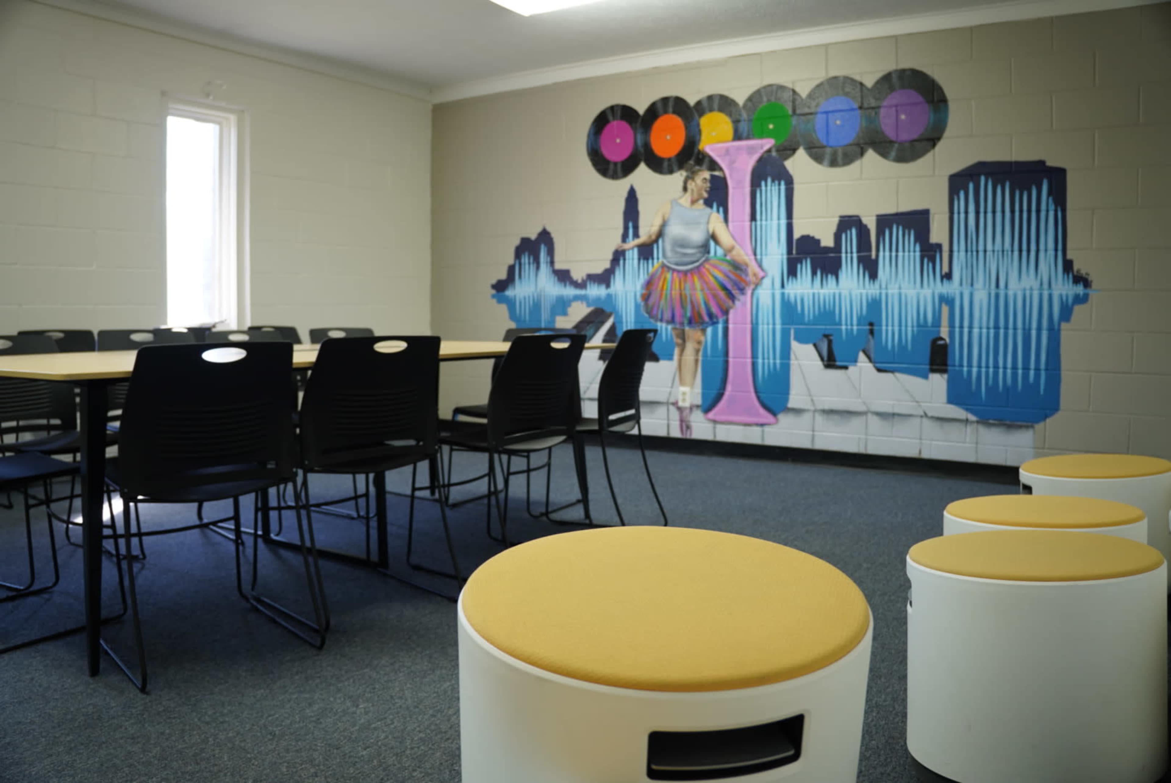 A conference room with a large mural of a woman dancing, surrounded by circular records and soundwave graphics, and a set of round seating stools.