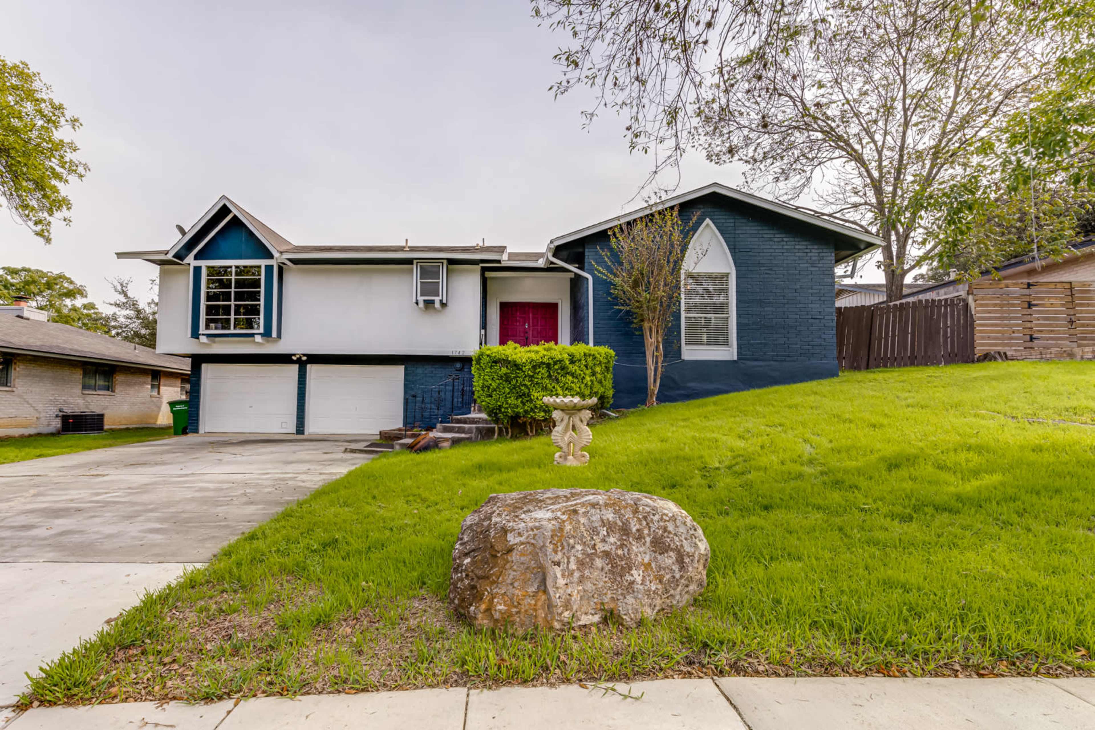 A single-story house with a split facade, featuring a blue and white exterior, a front lawn, and a large rock in the foreground.