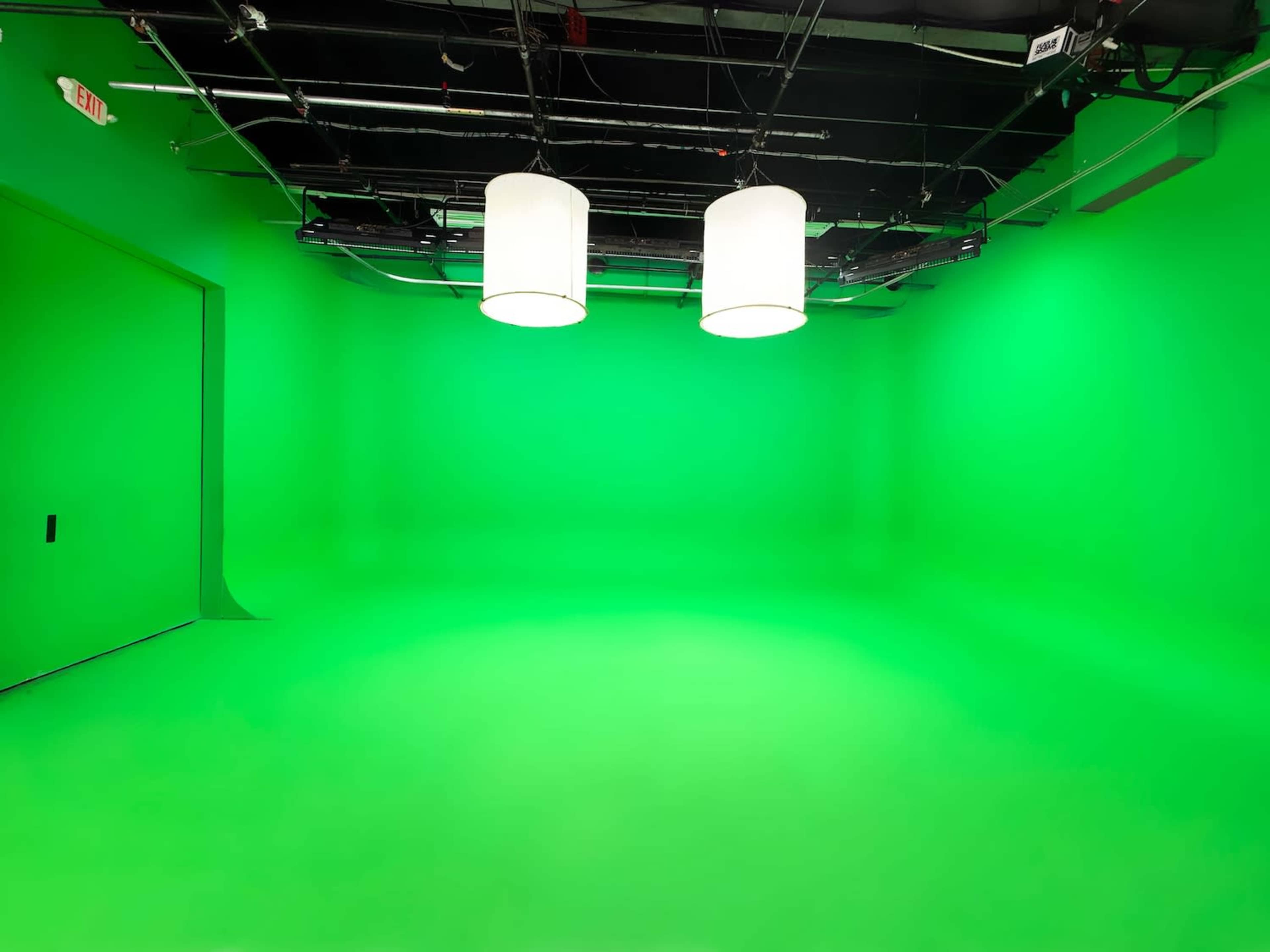 The image depicts a green screen studio with two large pendant lights hanging from the ceiling.