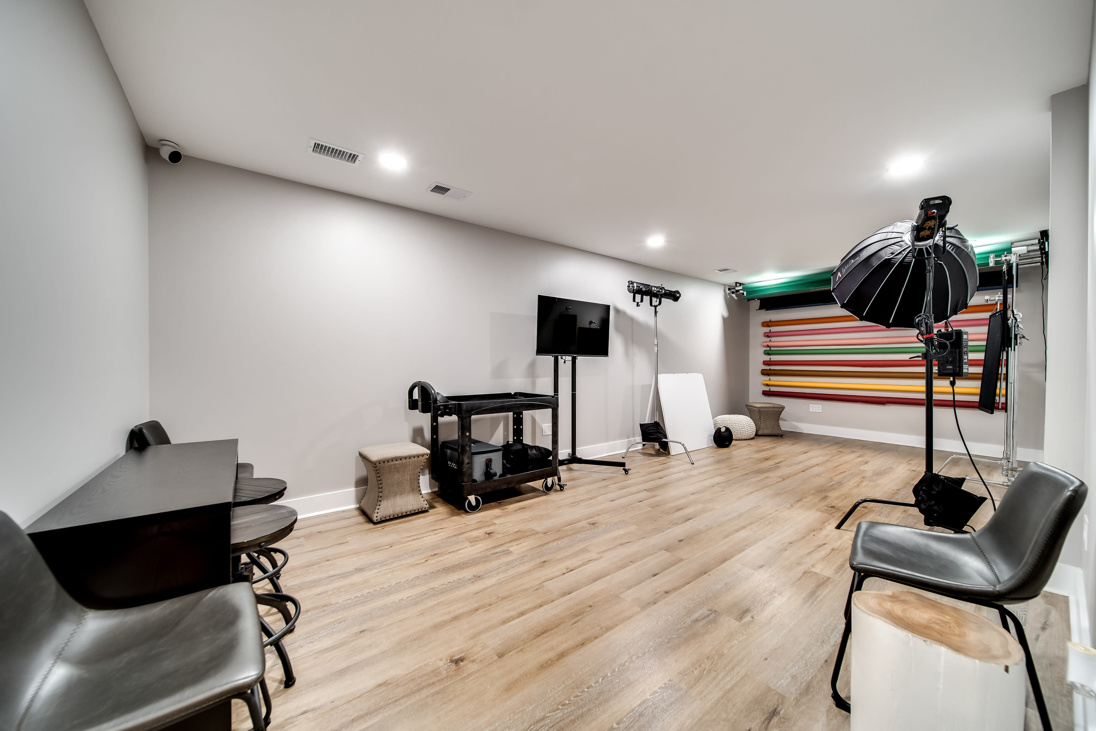 The image shows a photography studio with a large backdrop, lighting equipment, and seating arranged along the walls.