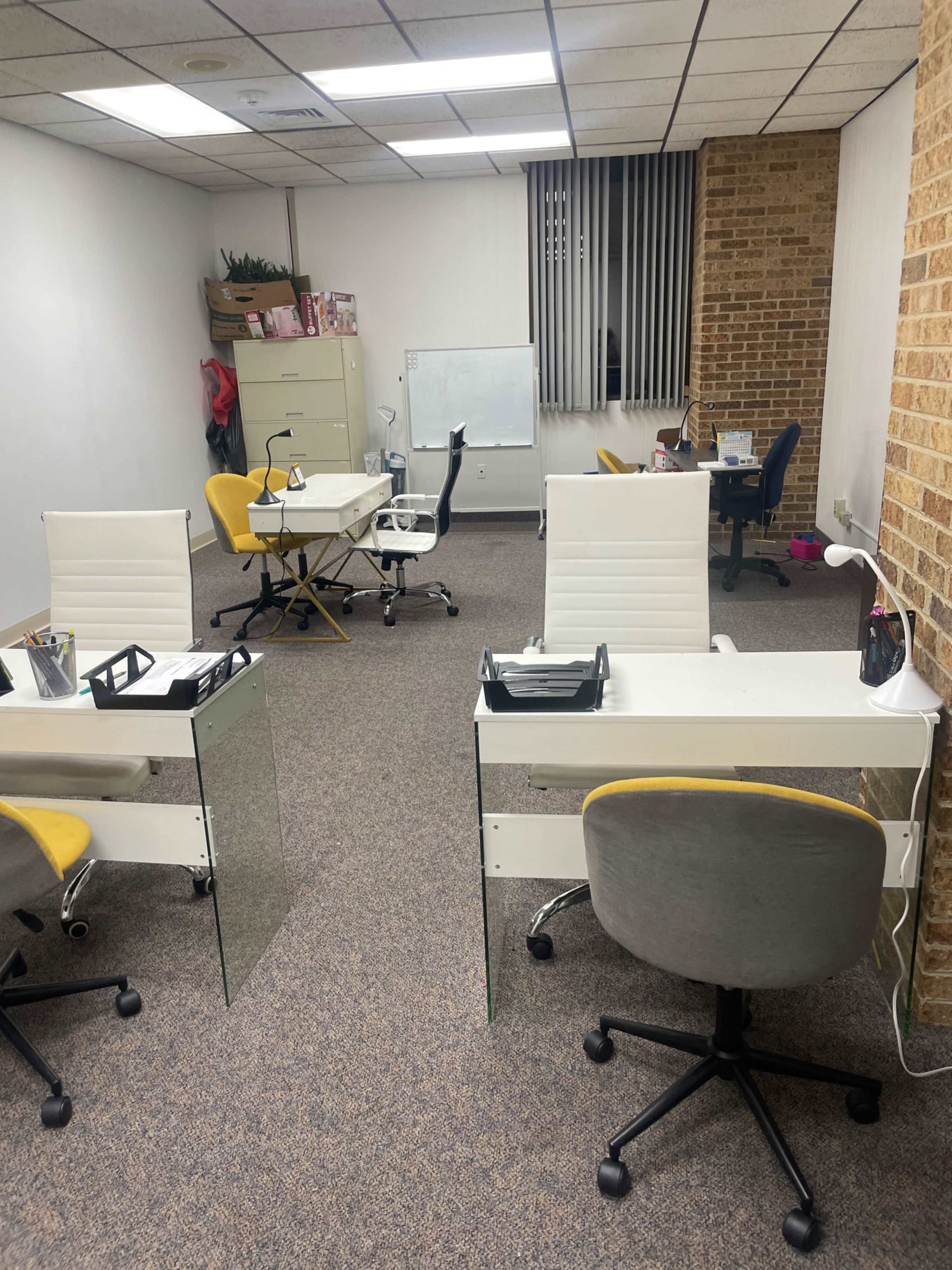A modern office space with multiple desks, each equipped with chairs, and a whiteboard at the far end.