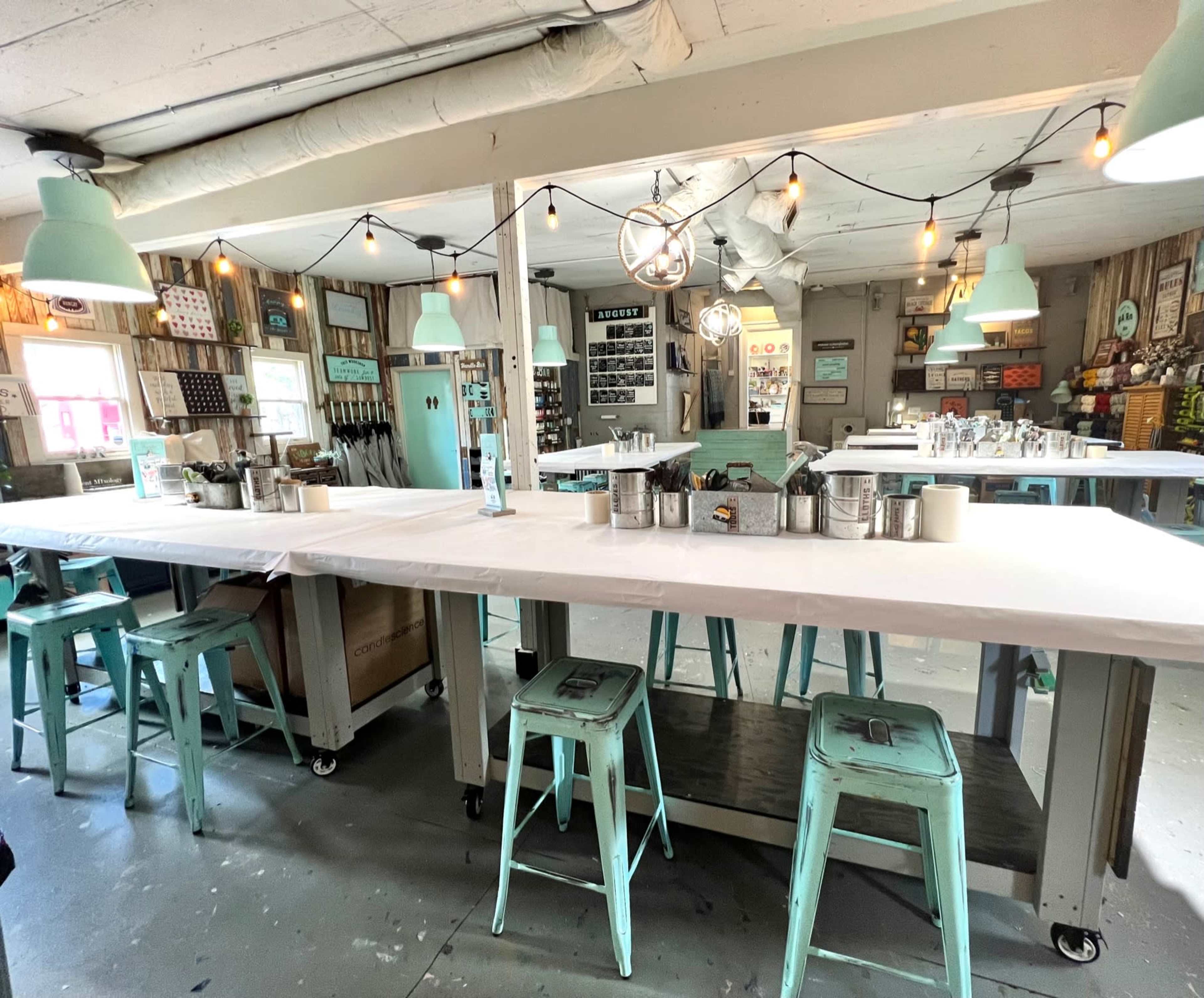 A spacious room with multiple worktables, teal stools, and pendant lights, designed for creative activities.