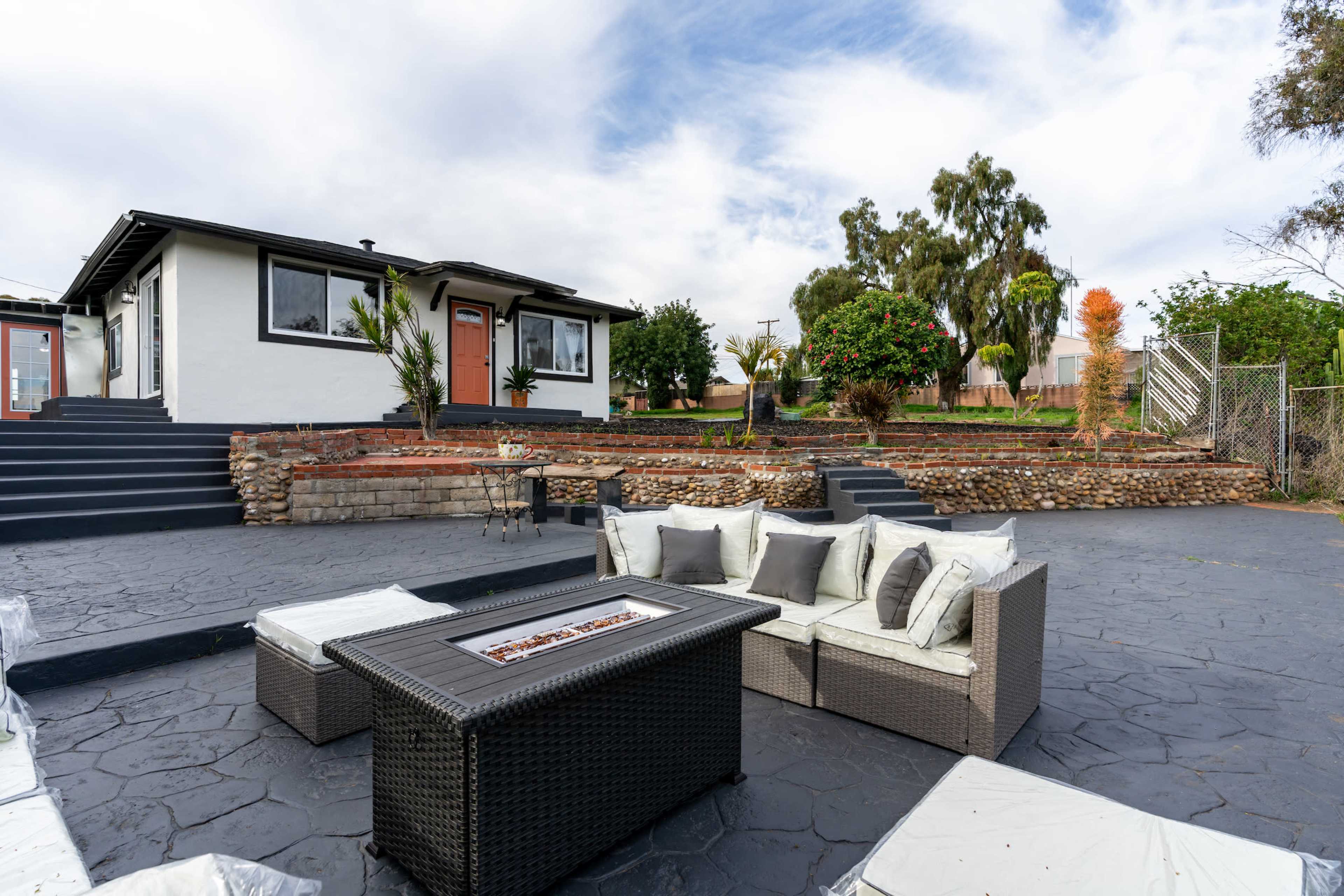 The image shows a landscaped outdoor patio area with a seating arrangement and a house in the background.