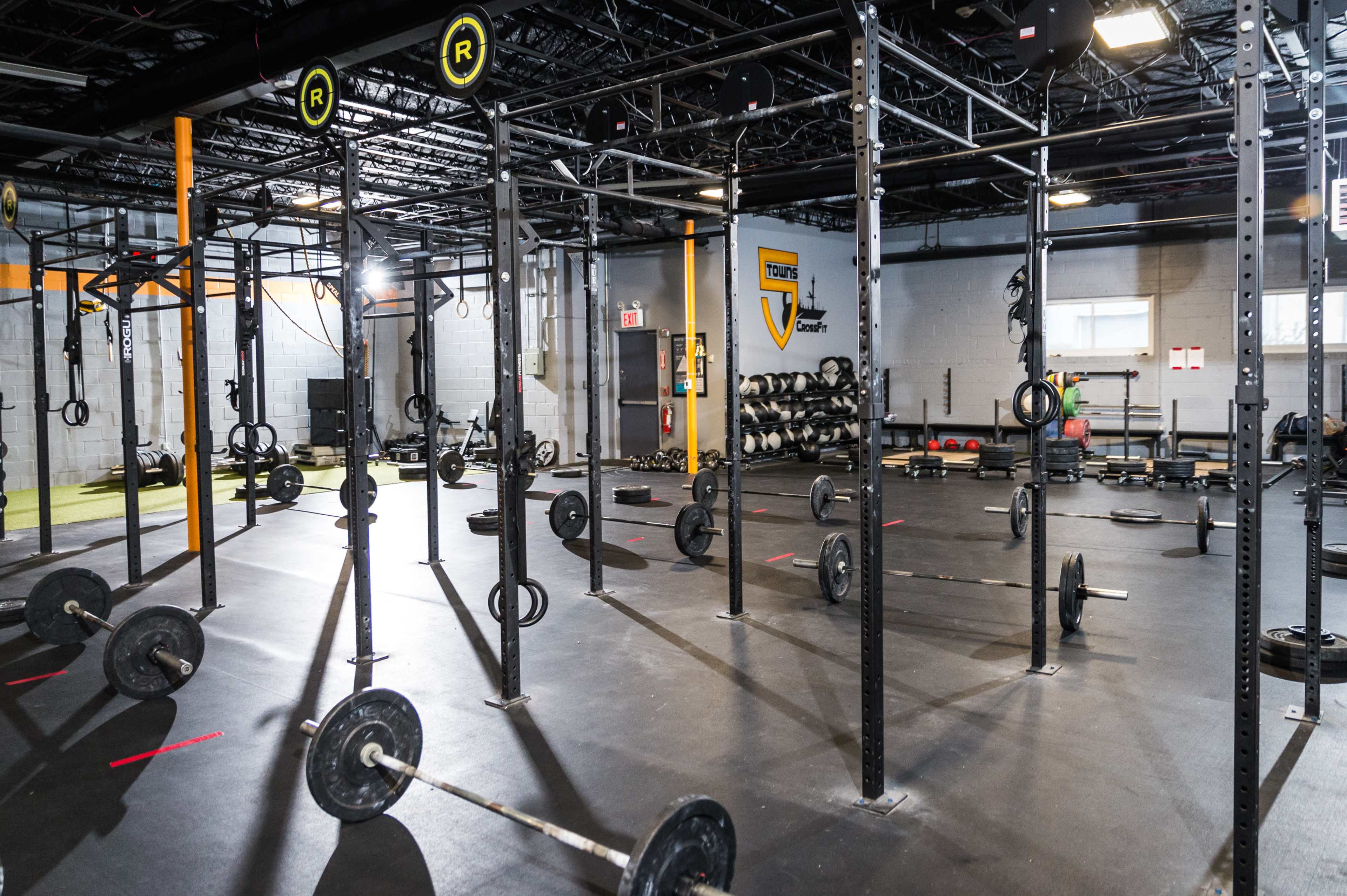 The image shows a spacious gym with multiple weightlifting stations, including barbells and squat racks, arranged on a black floor.