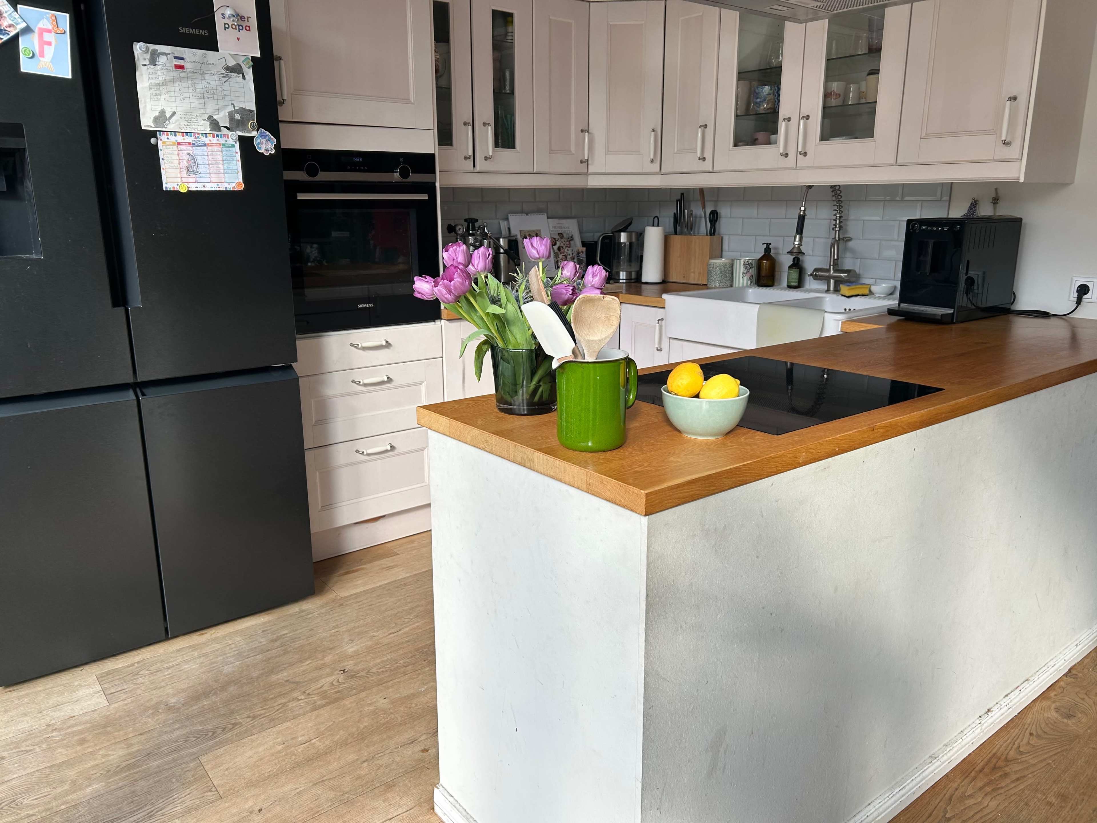 The image shows a modern kitchen with a central island, featuring a vase of tulips, cooking utensils, and a bowl of lemons on the countertop.