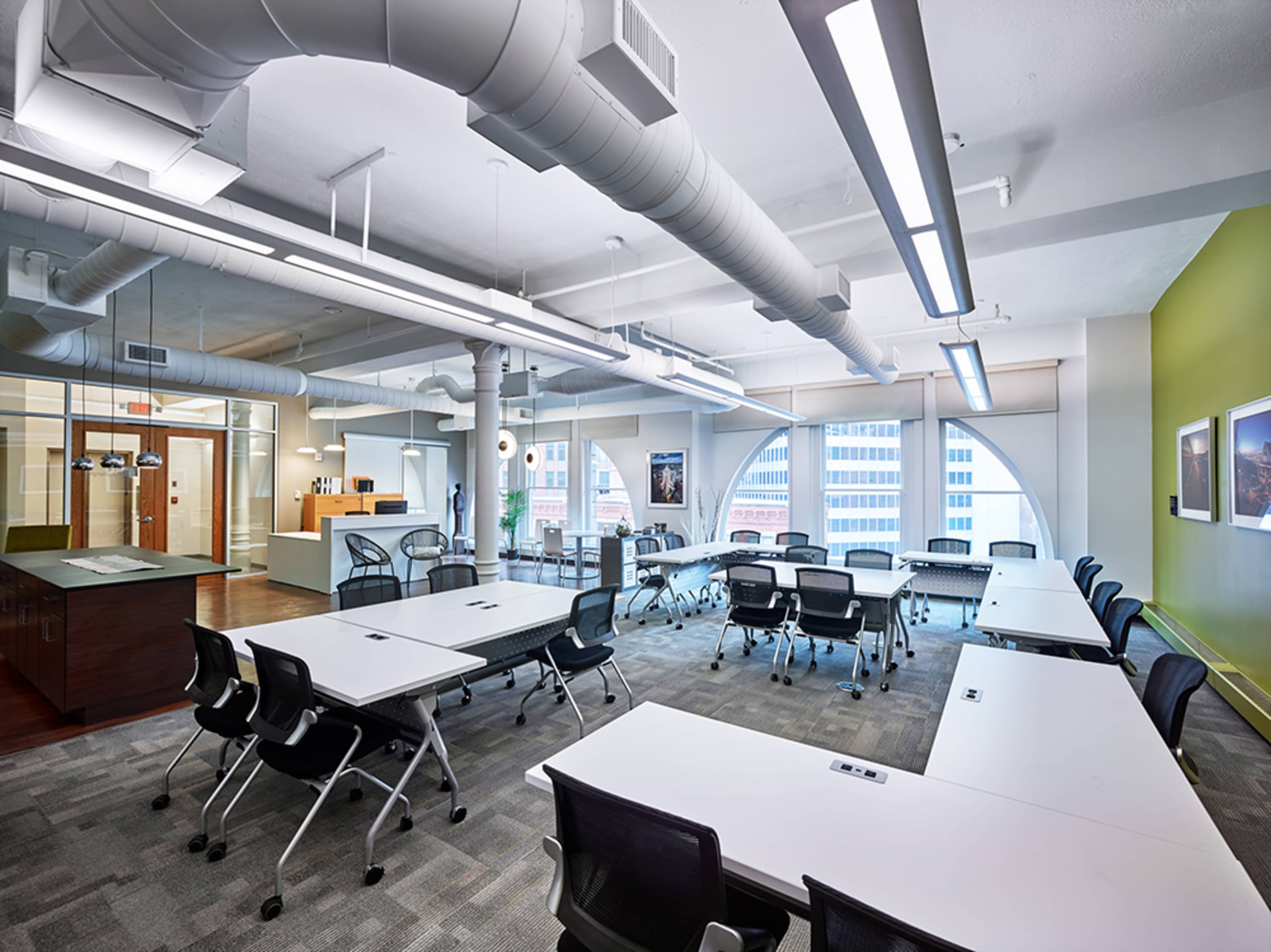 A modern office space with multiple tables arranged for meetings, surrounded by large windows and contemporary furnishings.