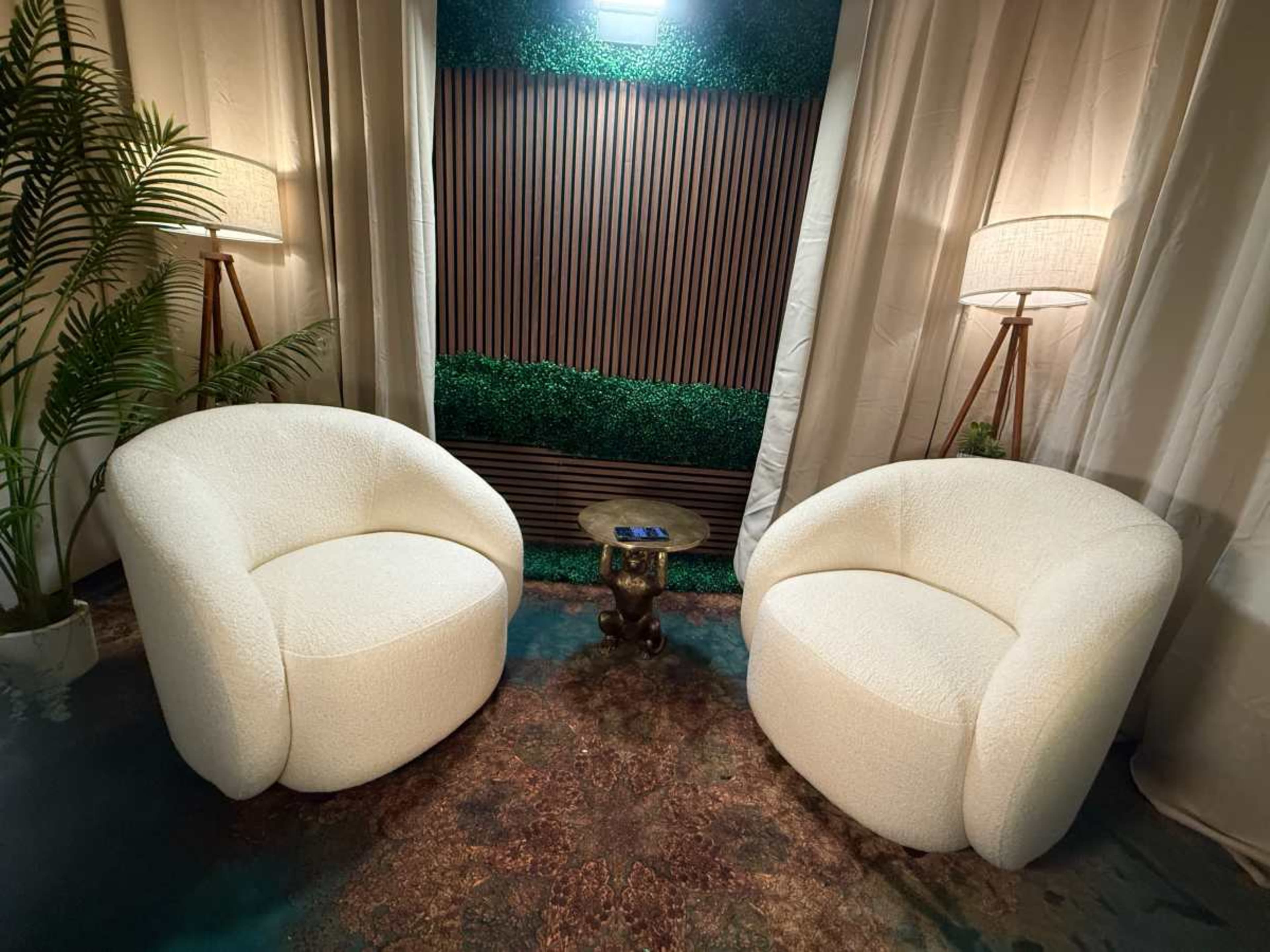 The image shows two round, cream-colored chairs positioned opposite each other in a setting with a wooden wall and soft lighting.