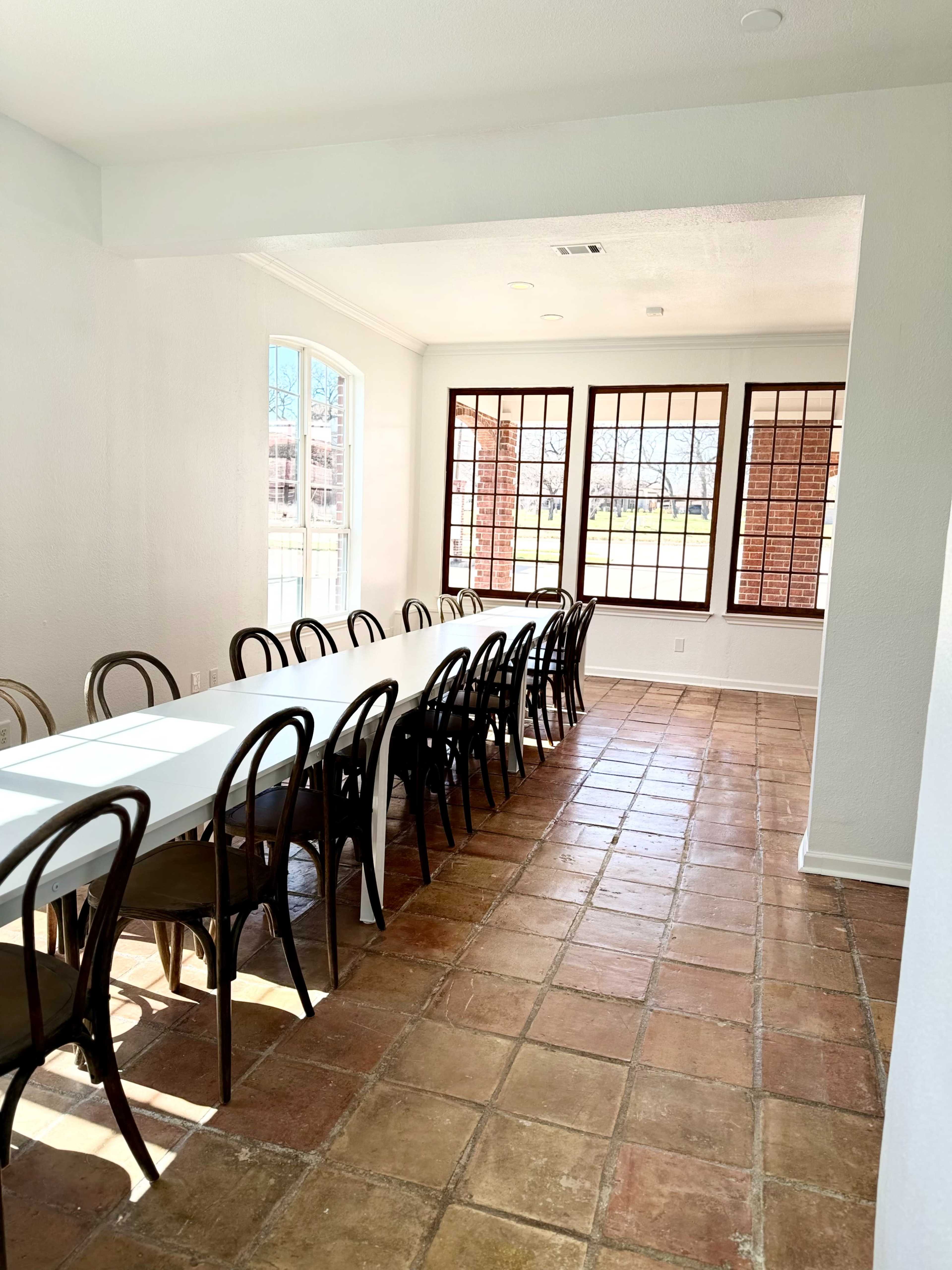 A long table is set up in a bright room with large windows and tiled flooring.