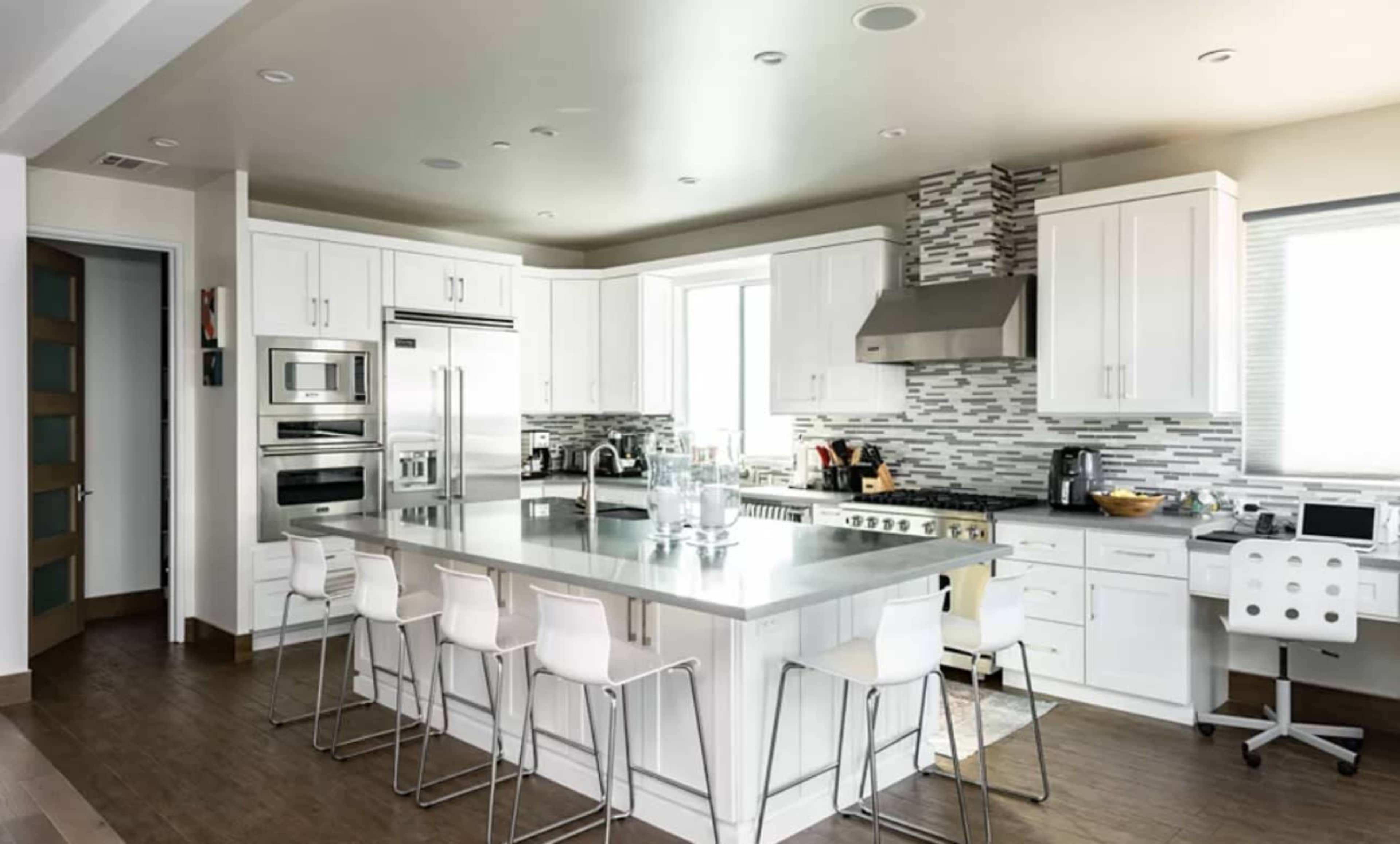 A modern kitchen features white cabinetry, stainless steel appliances, and a large island with bar seating.
